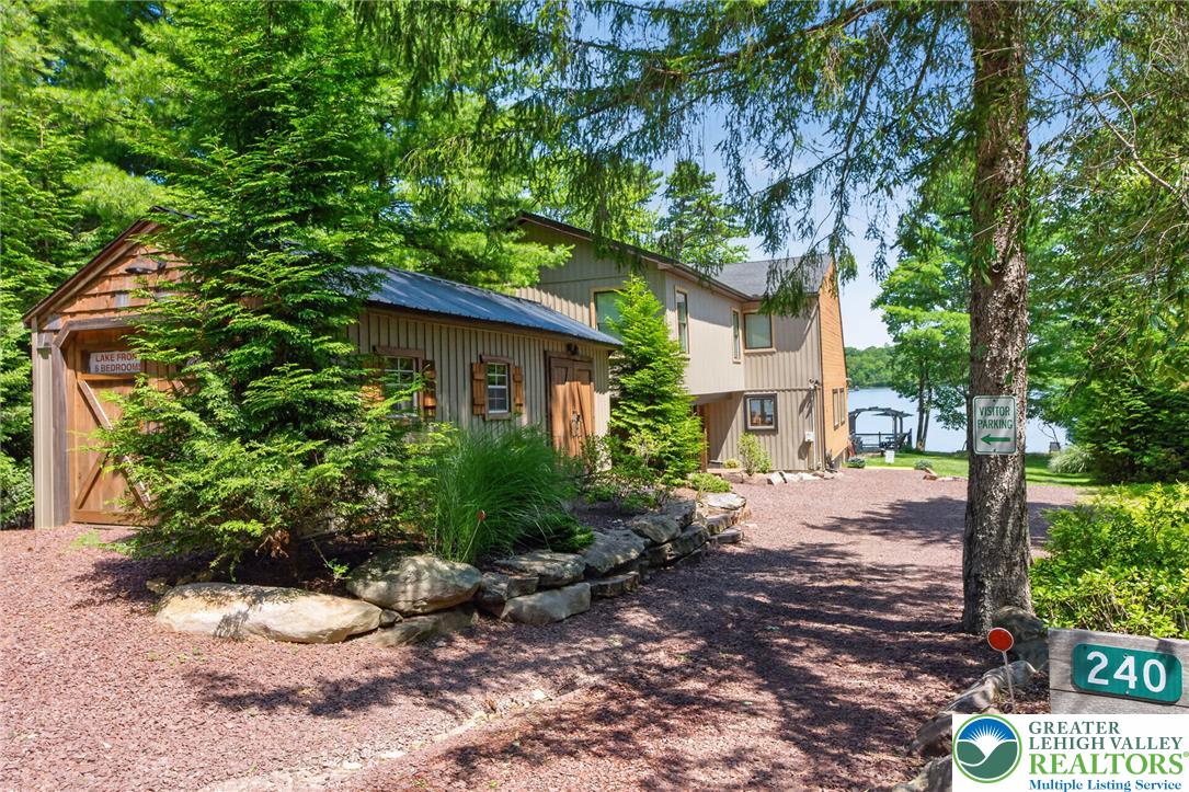 Lakefront home at 240, partly screened by trees, with the lake visible beyond the driveway.