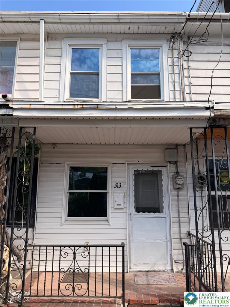 White-sided house front with covered porch, black iron railings, and the number 313 beside the door.