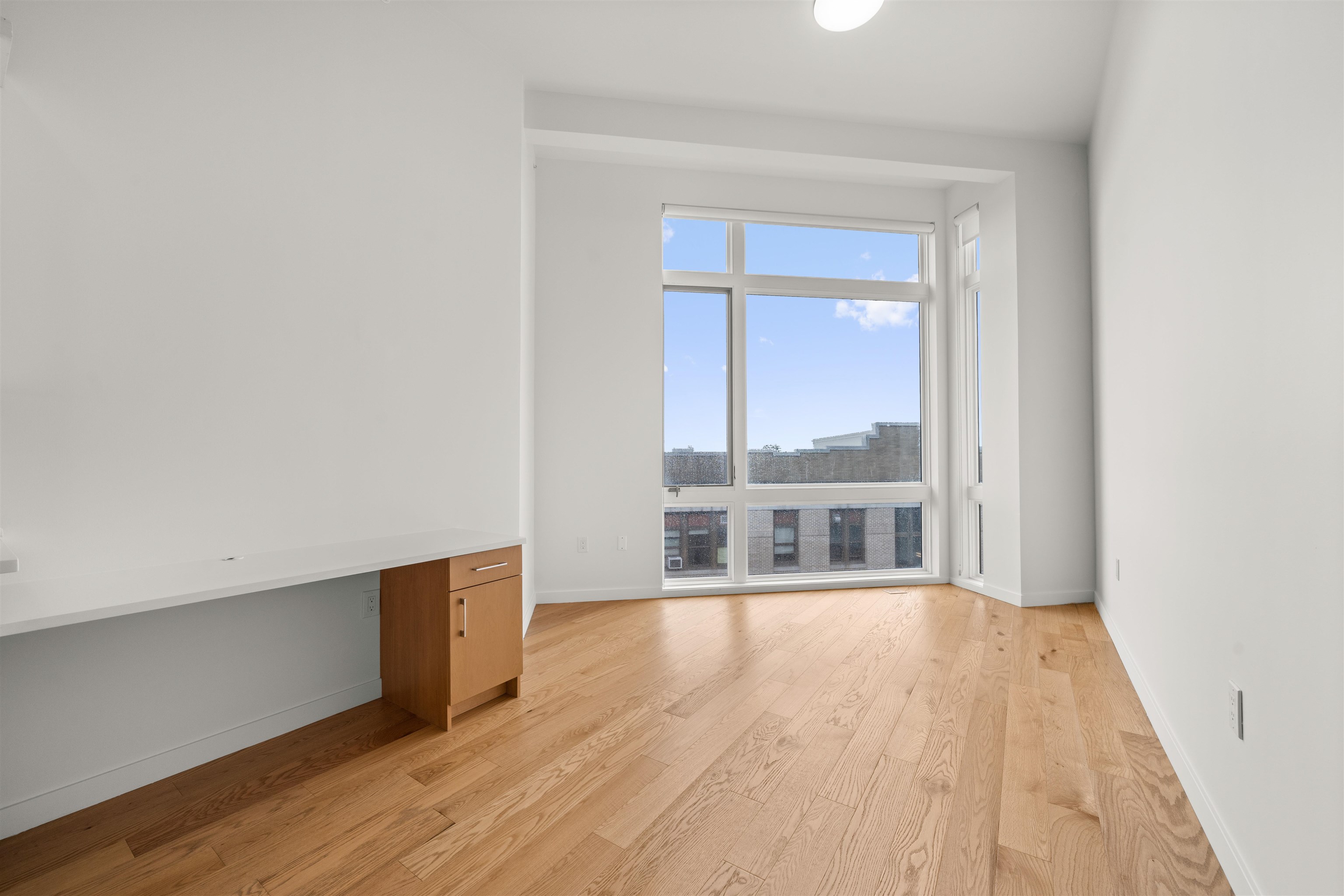 Vacant apartment room with hardwood floors, a built-in counter, and large corner windows.