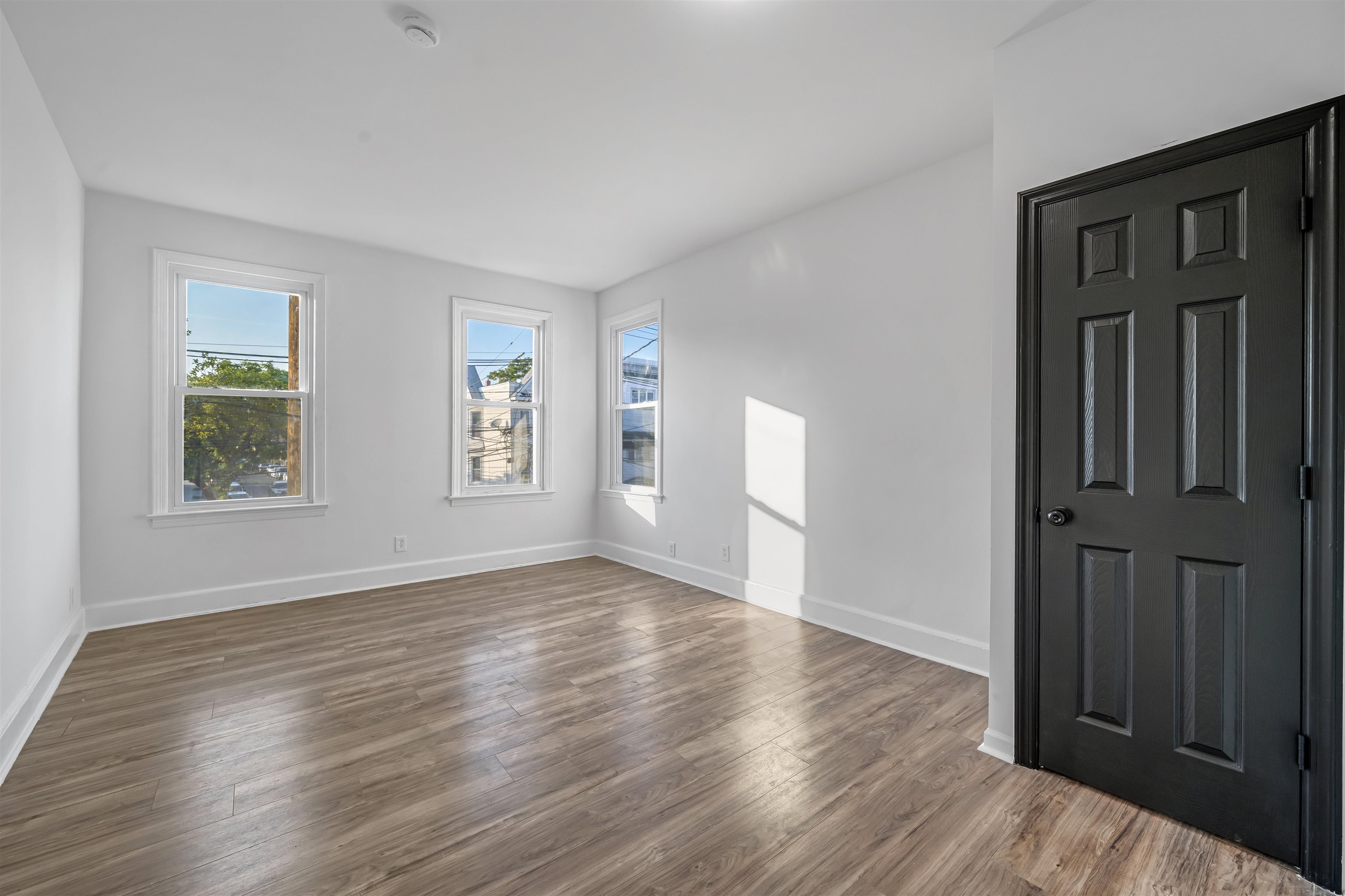Empty room with wood-look flooring, three windows, and a black paneled door.