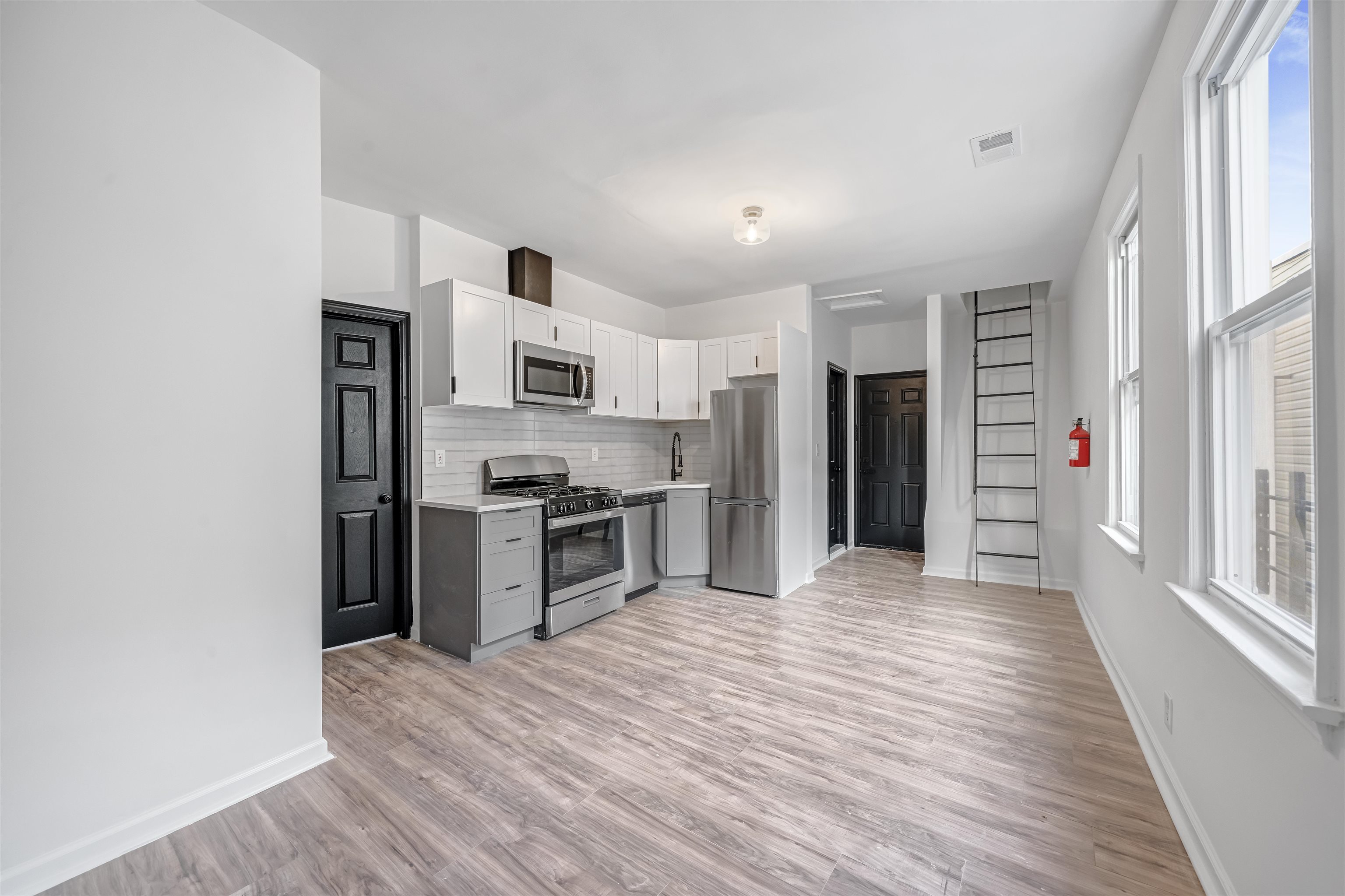 Vacant apartment kitchen with stainless steel appliances, white cabinets, and tall windows.
