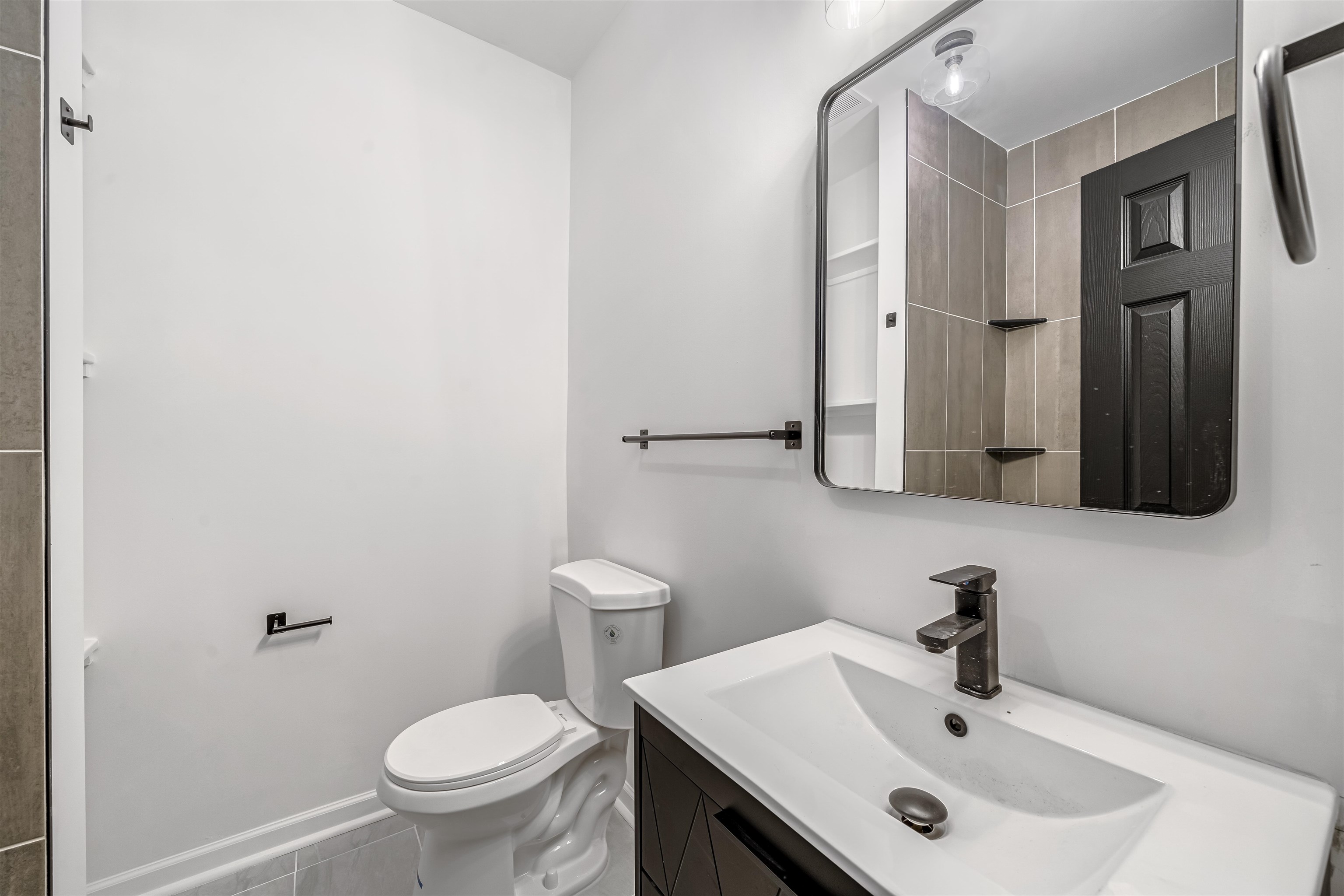 Bathroom with a dark wood vanity, wide white sink, and mirror reflecting tiled walls and a dark door.