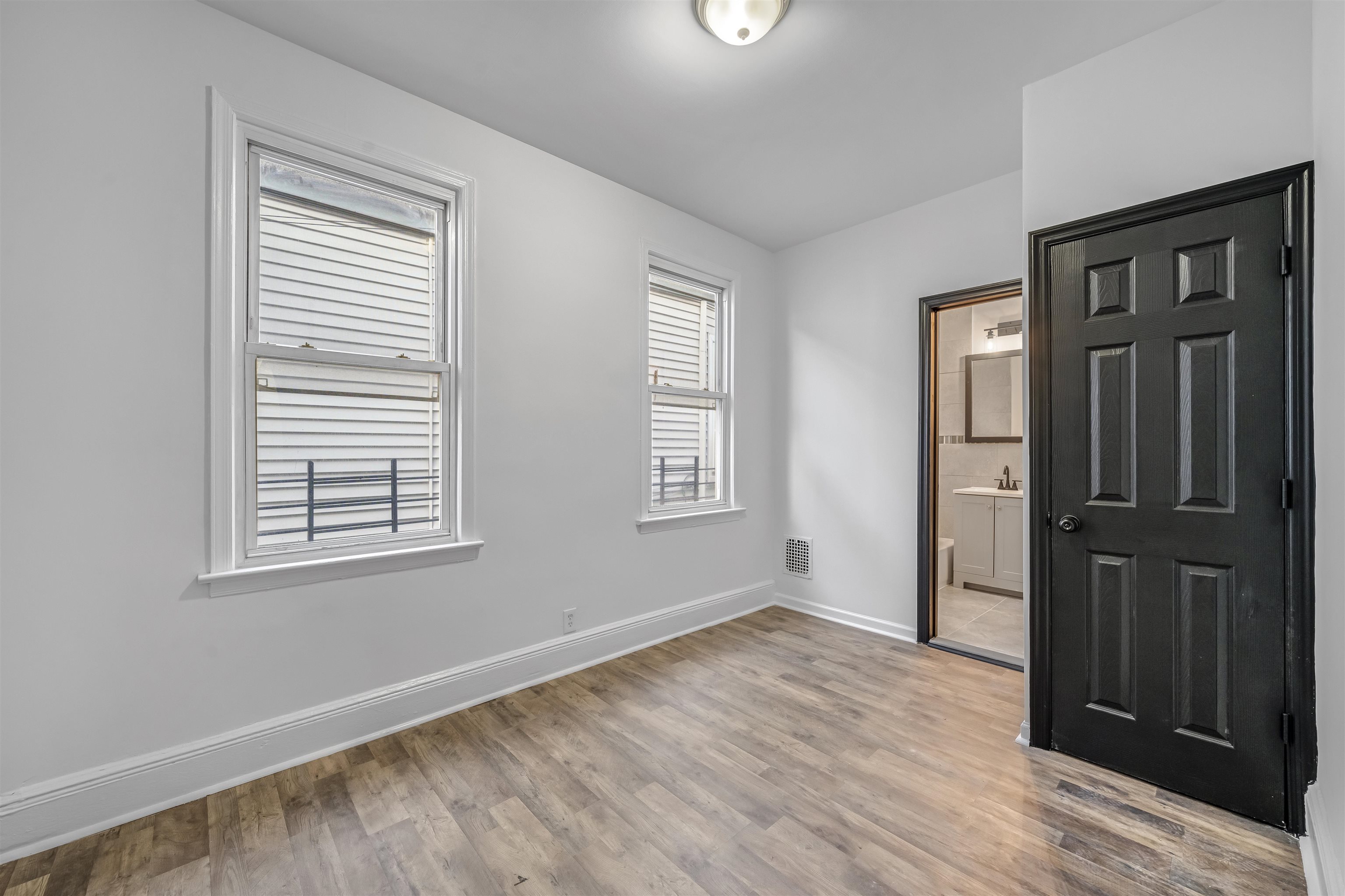 Empty room with wood-look flooring, two windows, and an open doorway to a bathroom.