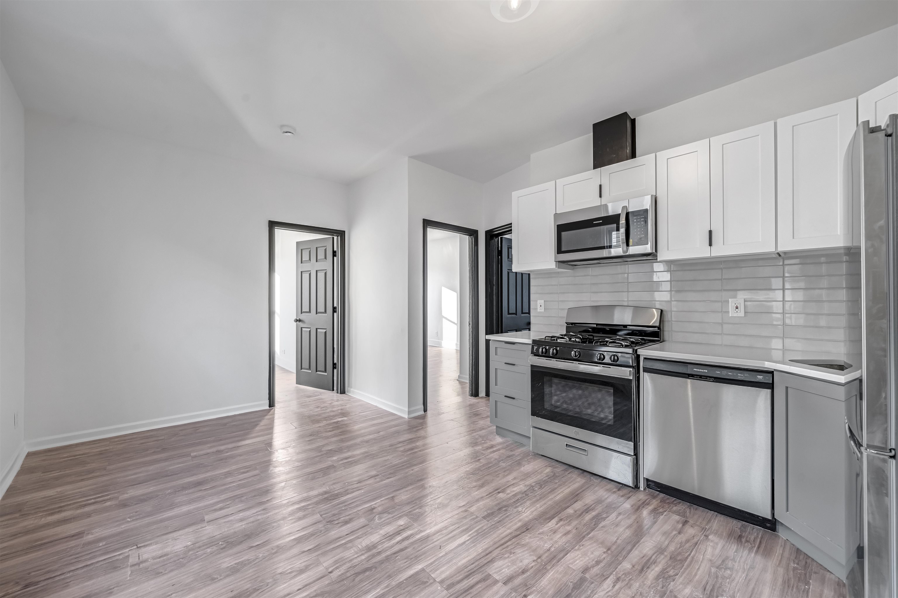 Vacant kitchen with white cabinets, stainless steel appliances, and wood-look flooring.