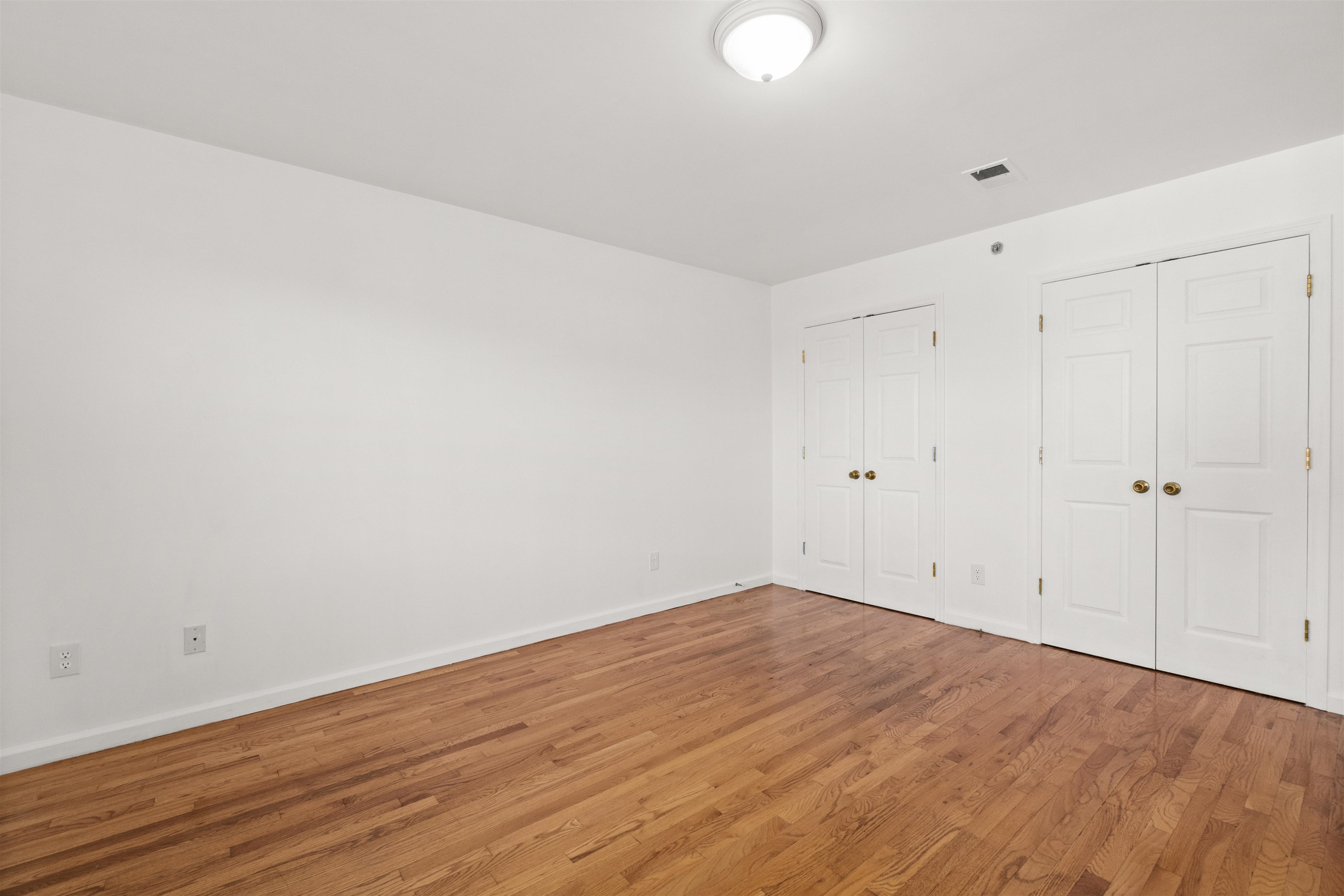 Empty room with hardwood floors and two sets of white closet doors.