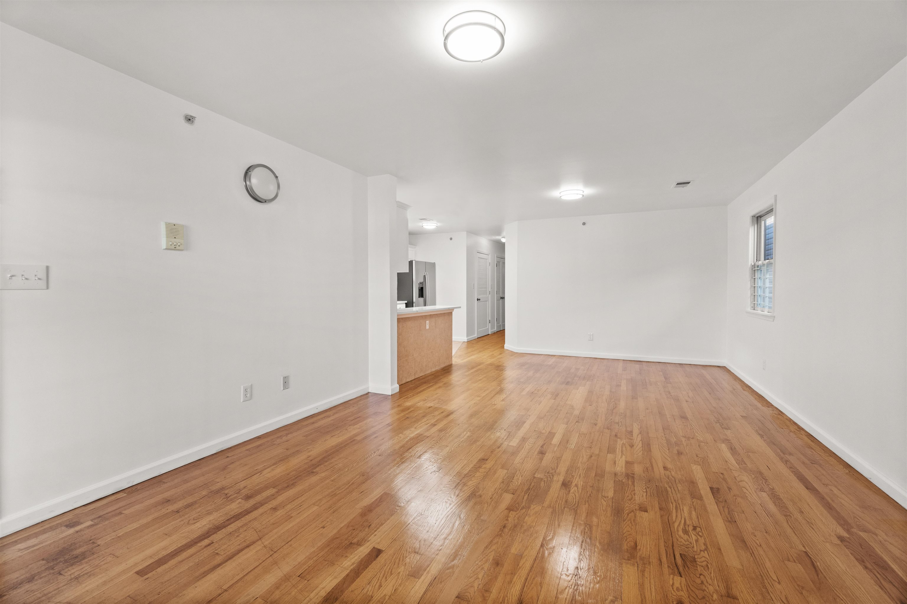 Vacant living and dining area with hardwood floors and a kitchen counter.