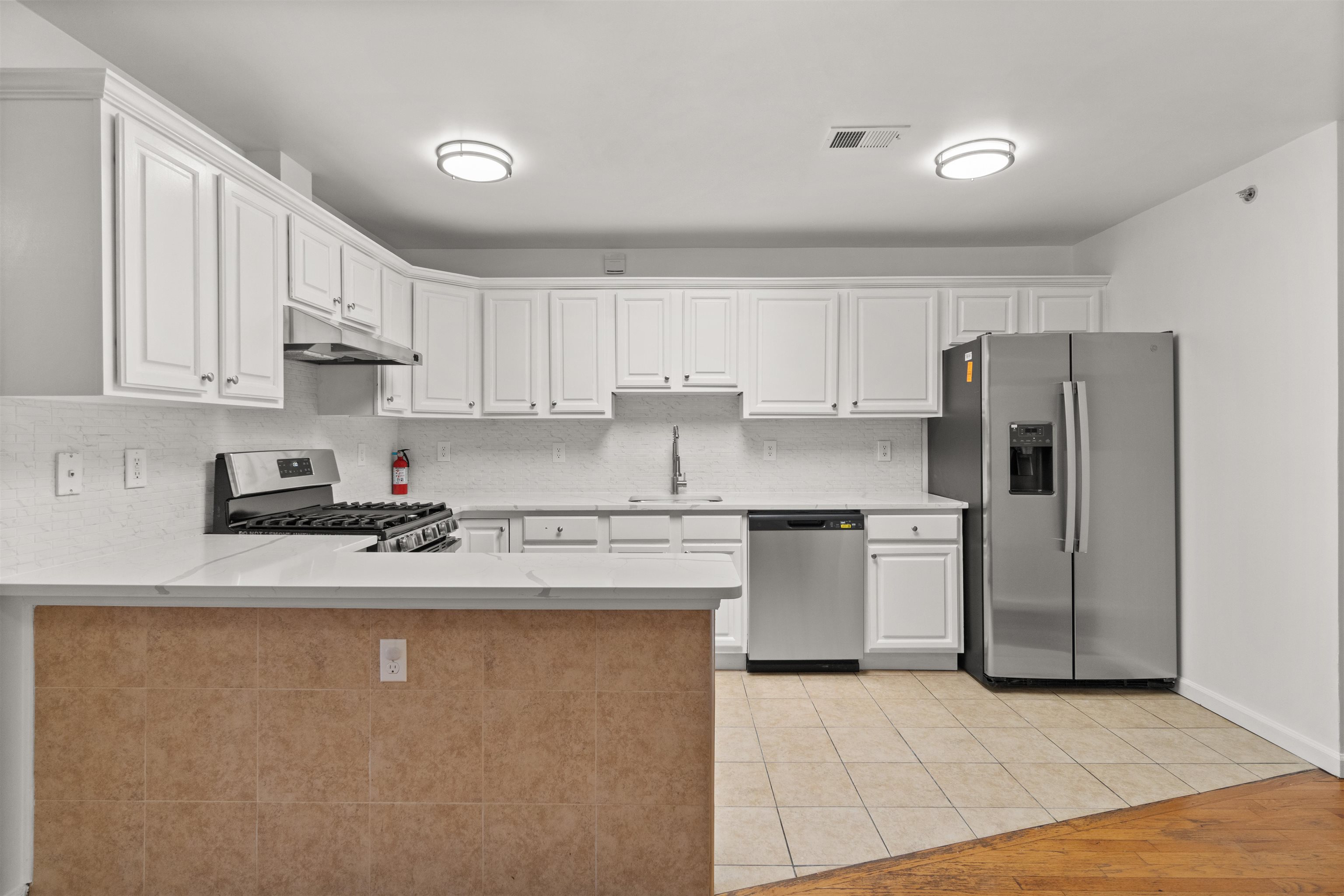Kitchen with white cabinets, stainless steel appliances, and a large tiled-front peninsula.