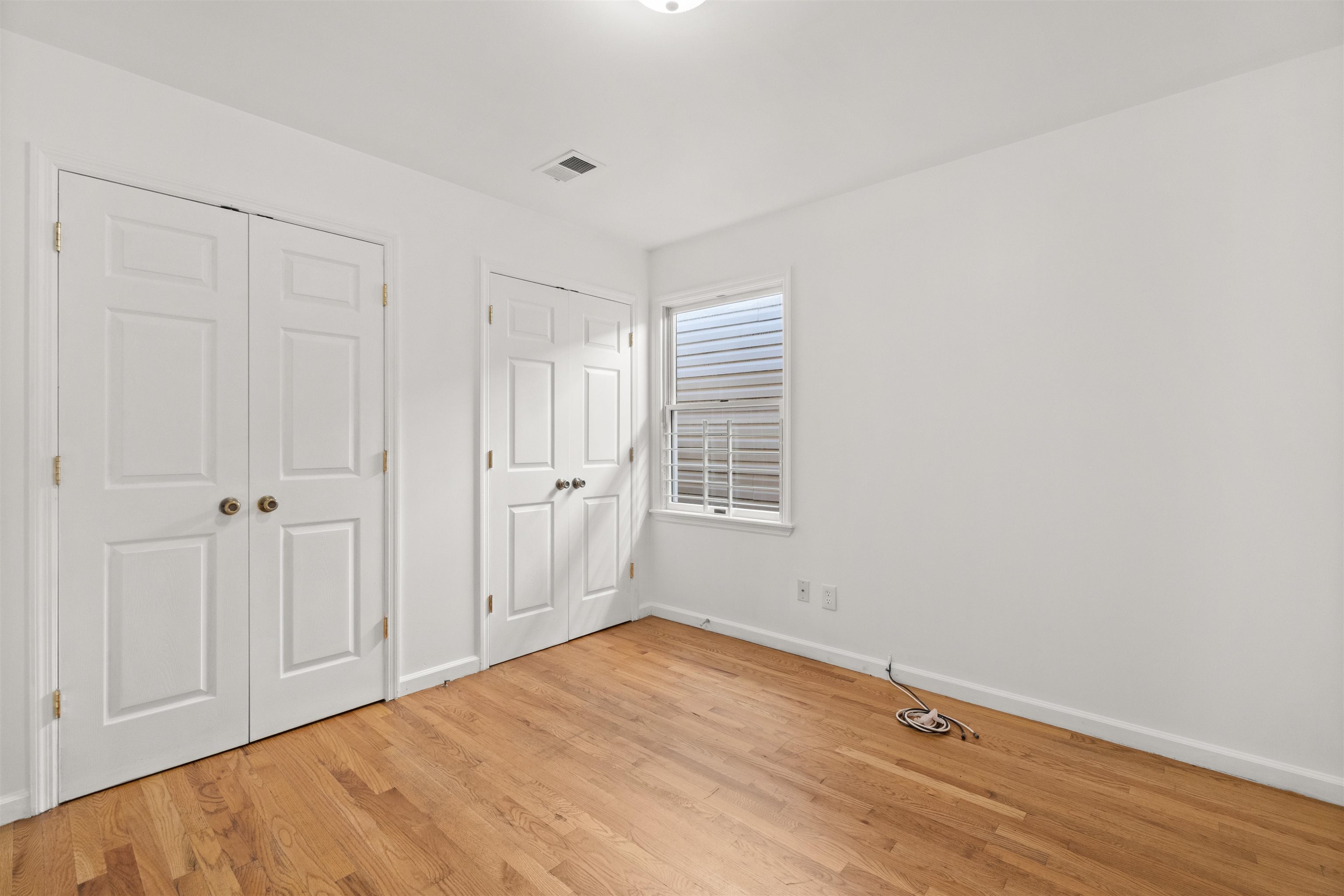 Empty room with hardwood floors, two closets, and a window with blinds.