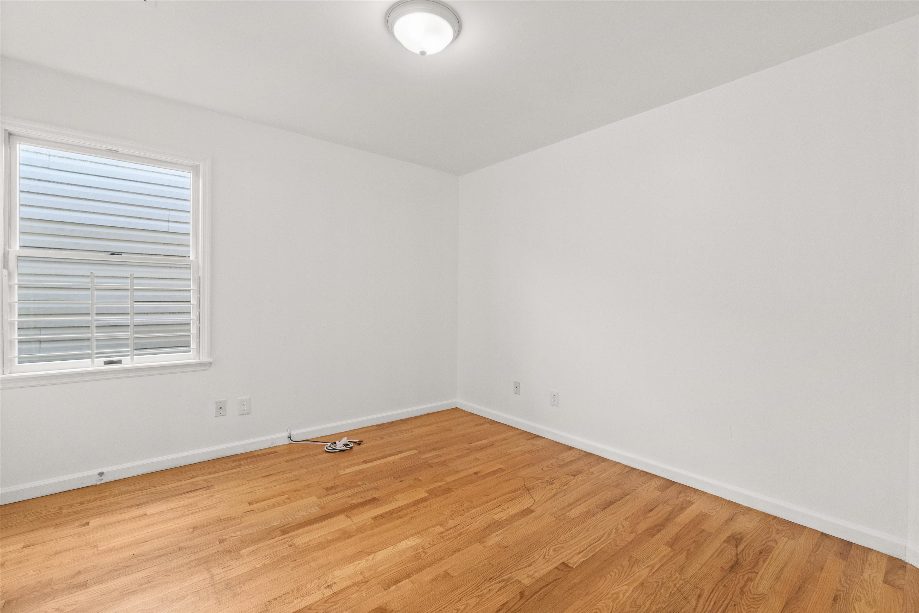 Empty room with hardwood floors and a large barred window with blinds.