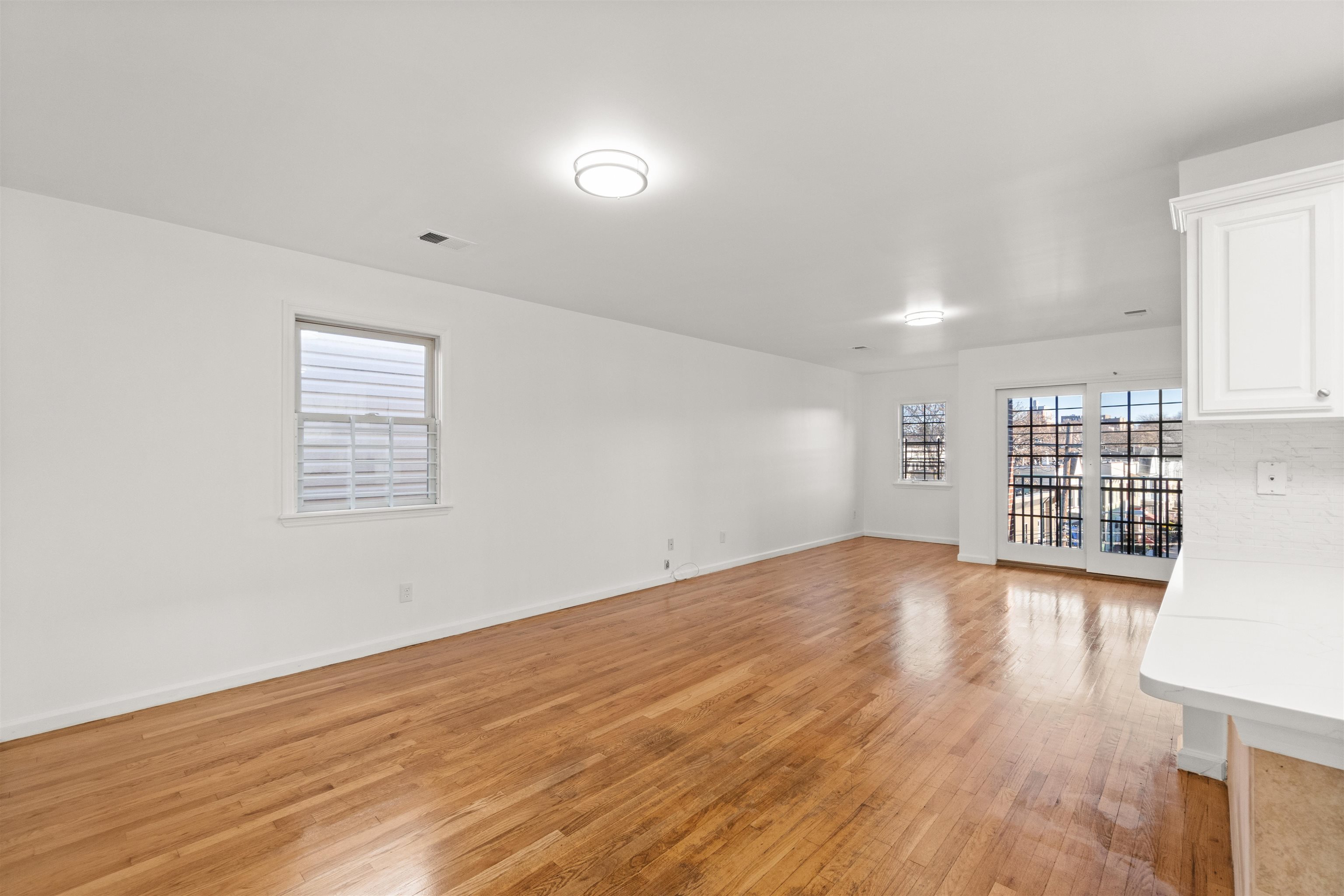 Vacant living room with hardwood floors, white walls, and glass doors at the far end.