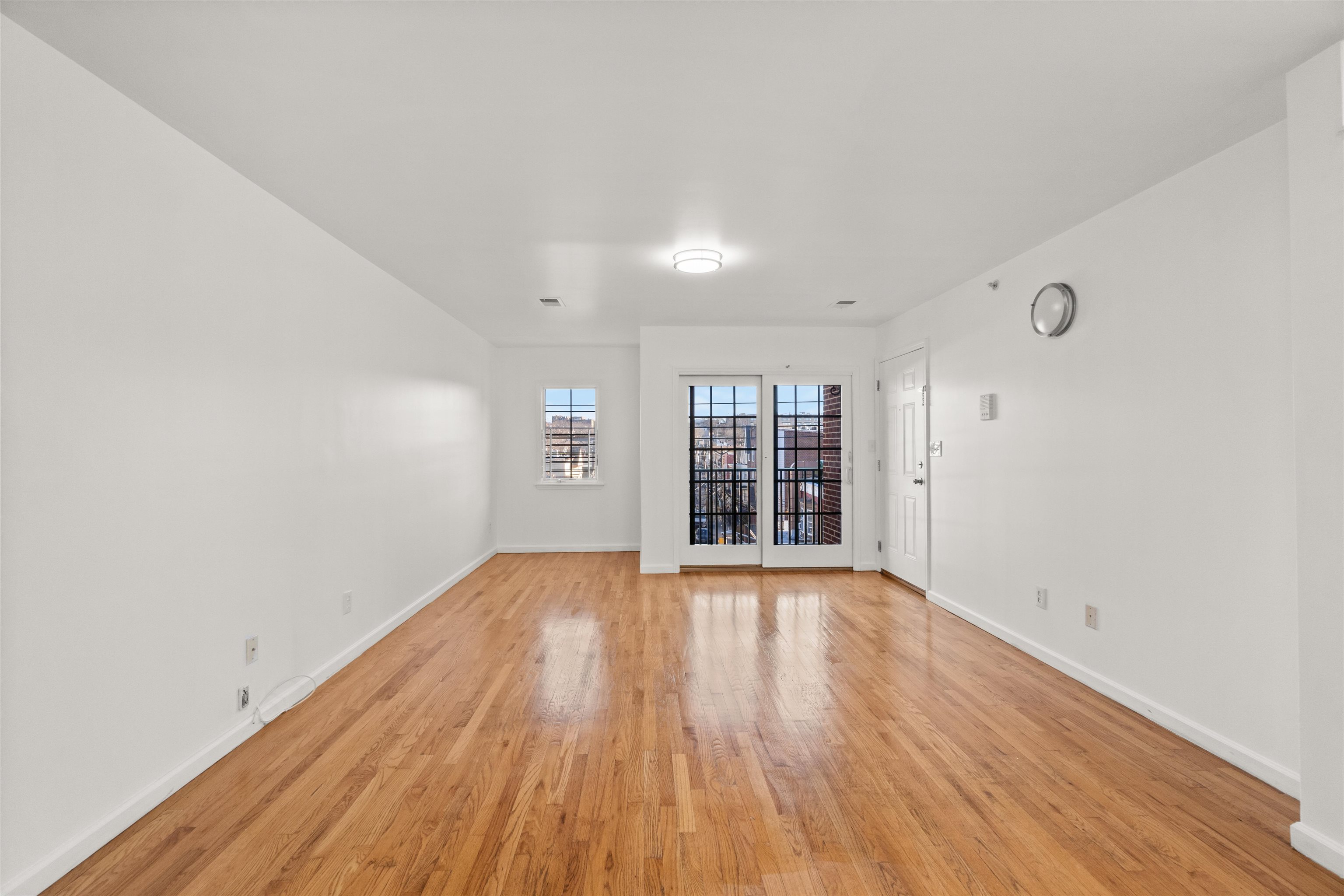 Vacant living room with hardwood floors and black-grid glass doors opening to a balcony.
