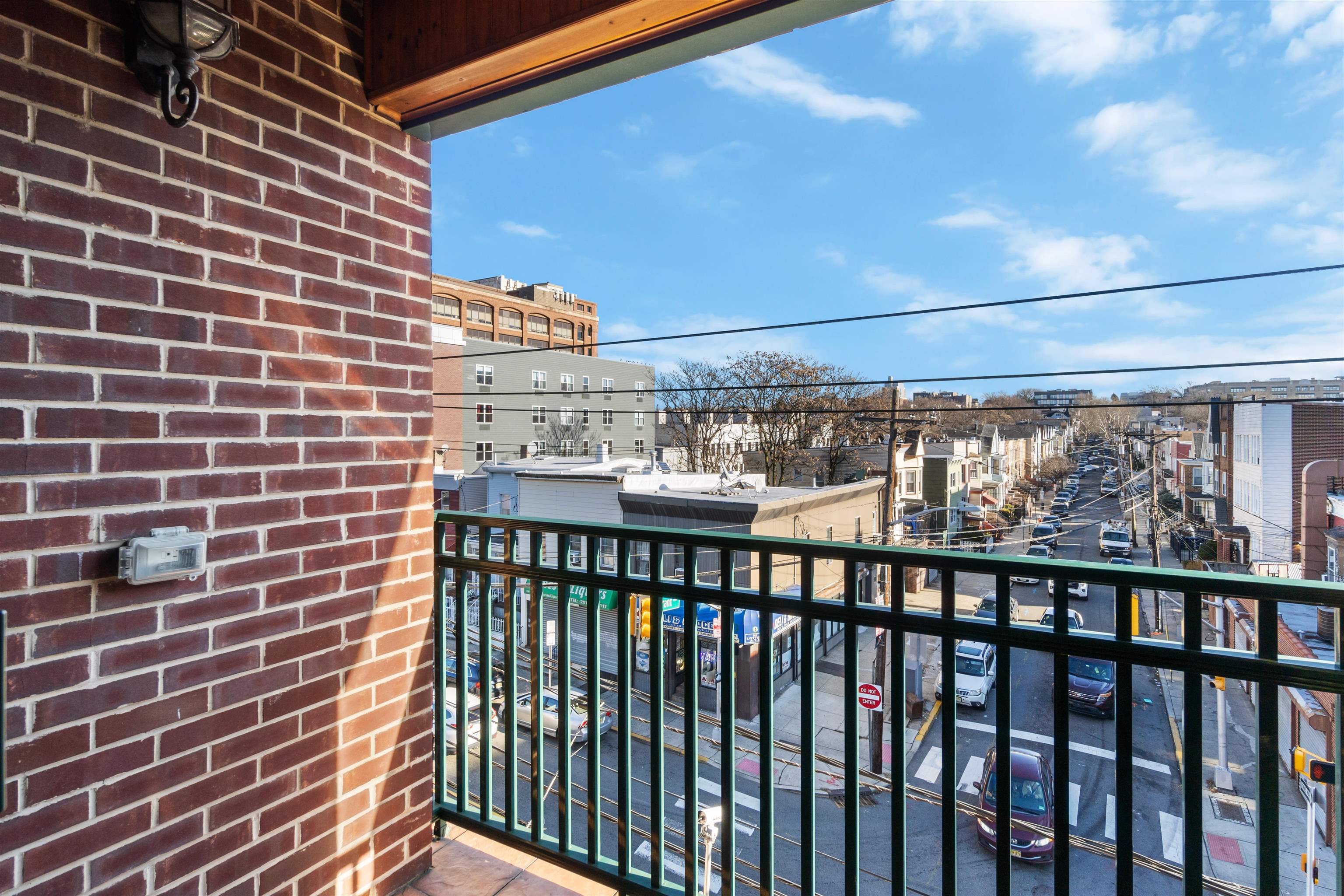 Covered balcony overlooking an urban street, with a brick wall and black metal railing.