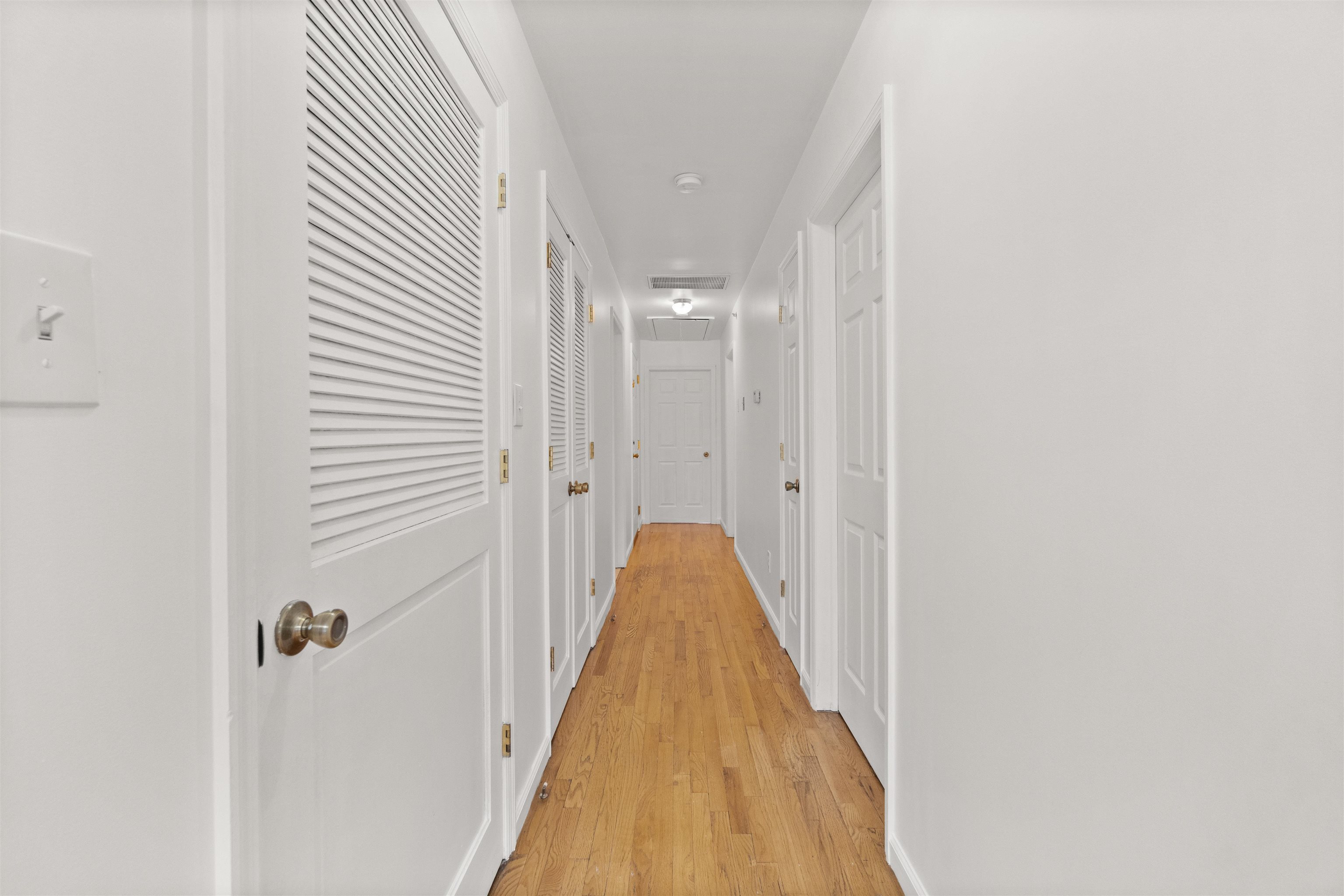 Hallway with white doors and louvered closets along honey-toned hardwood floors.