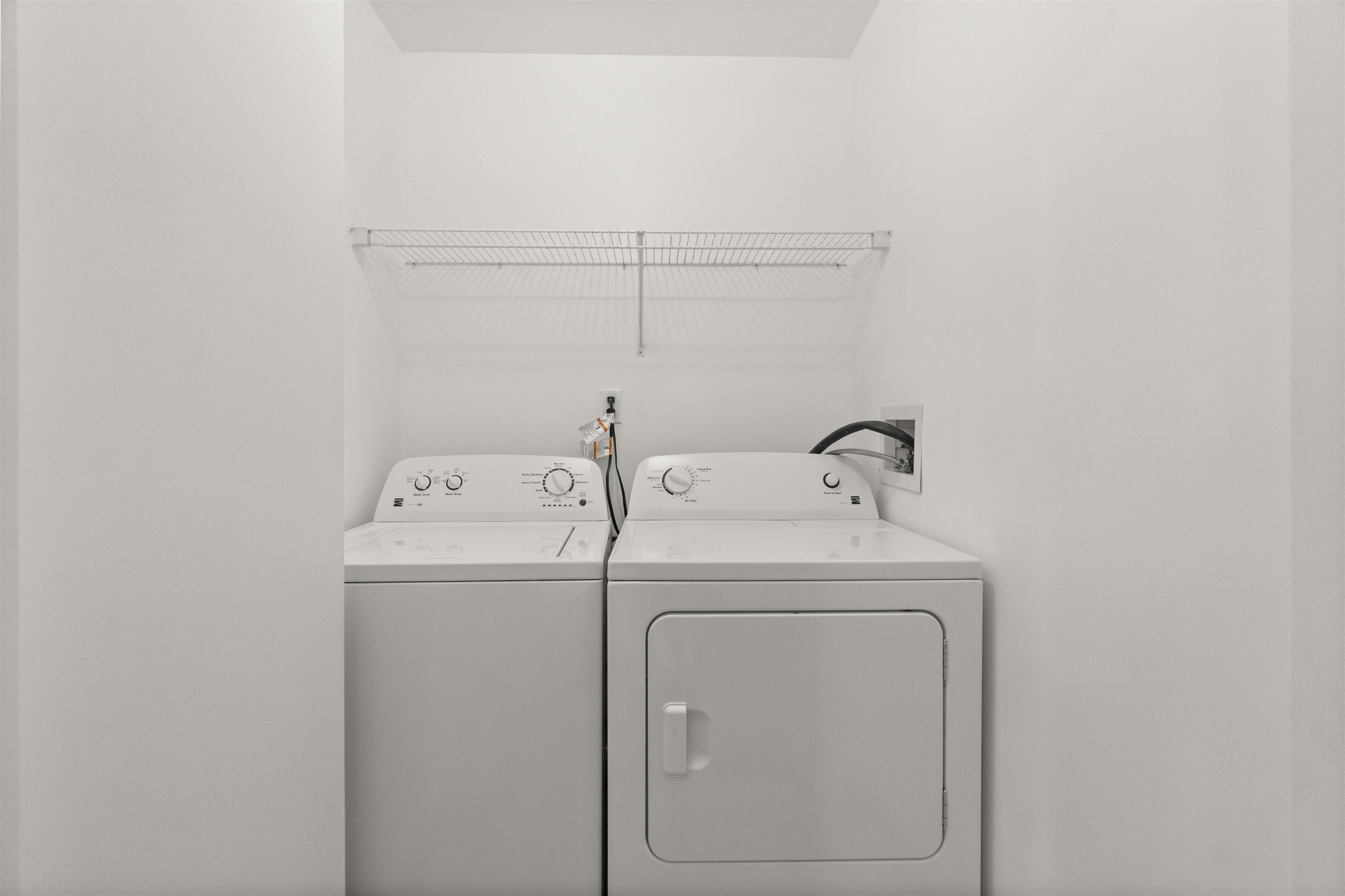 Laundry closet with side-by-side washer and dryer beneath a wire drying shelf.