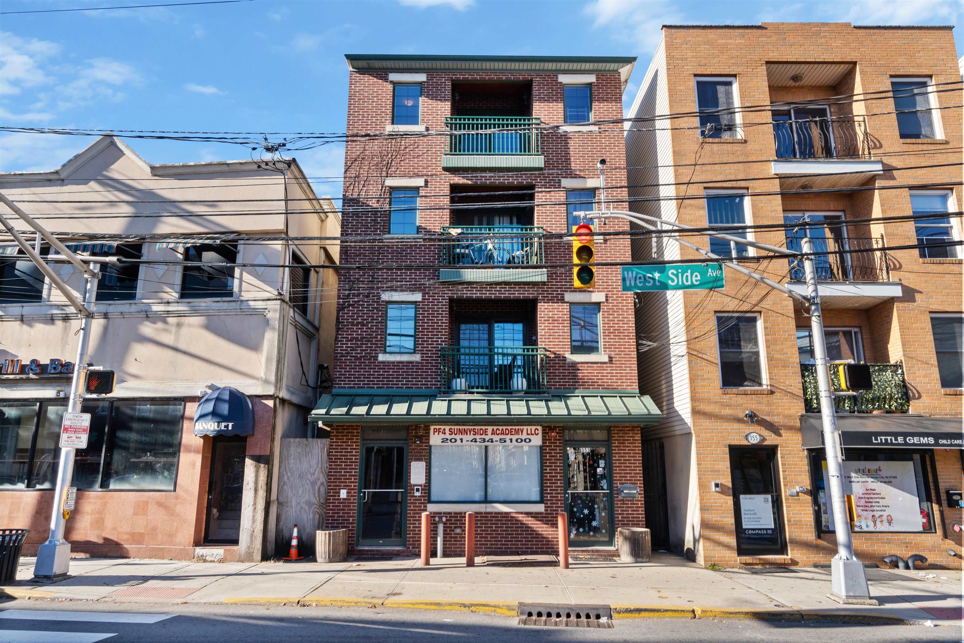 Red-brick multi-story building with green-railed balconies and an academy storefront on West Side Avenue.