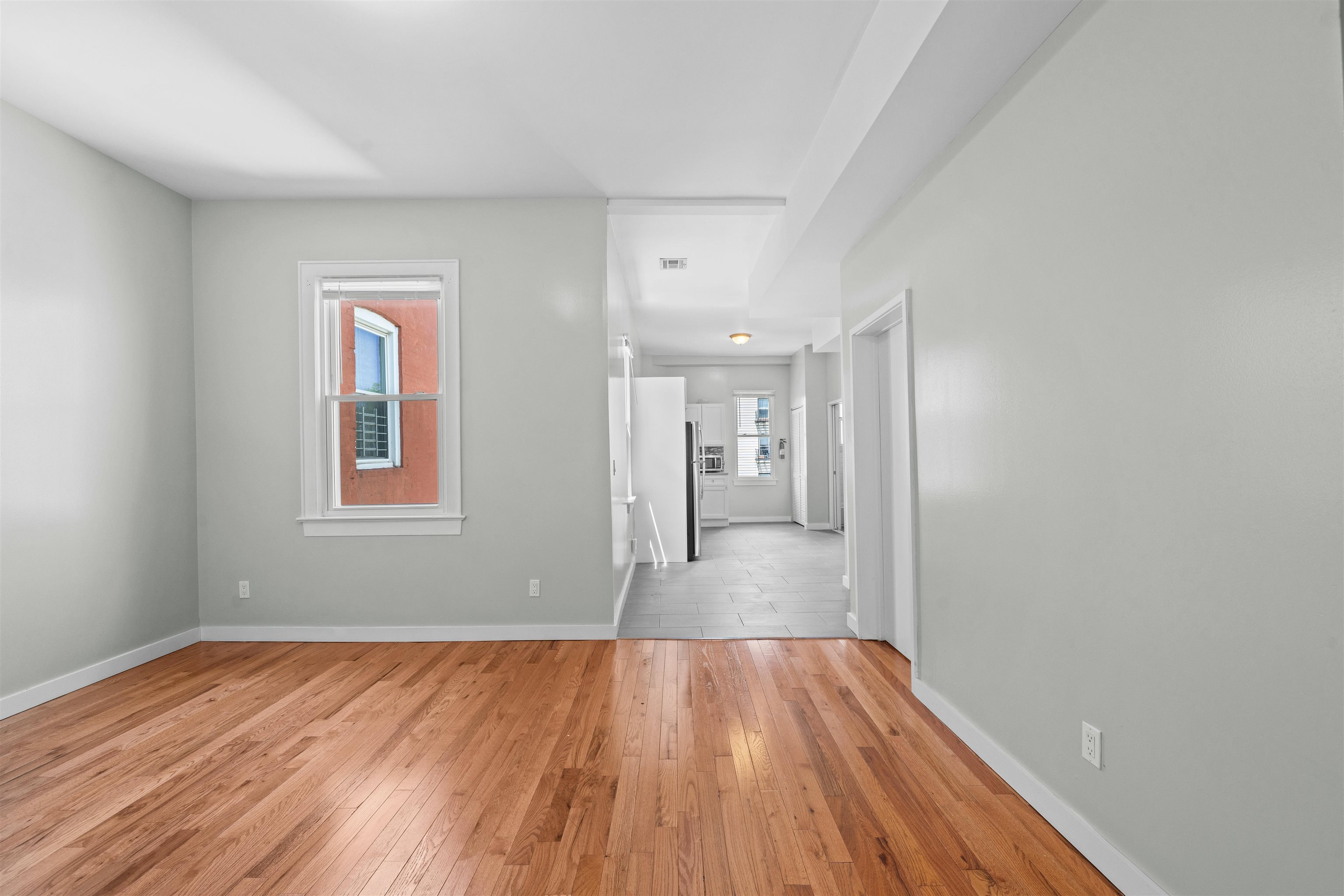 Vacant living area with hardwood floors opening to a tiled kitchen.