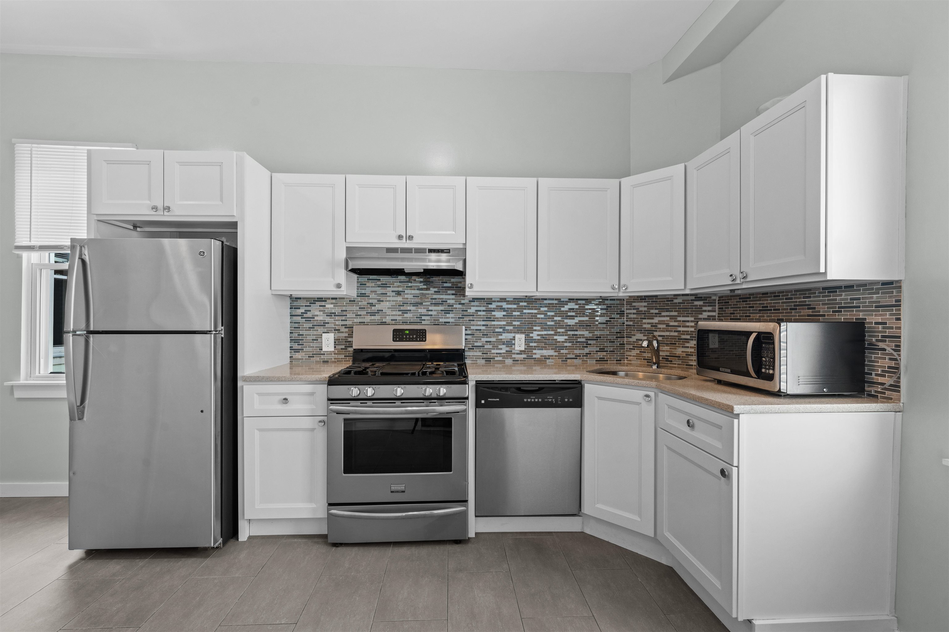 Kitchen with white cabinets, stainless steel appliances, and a multicolored tile backsplash.