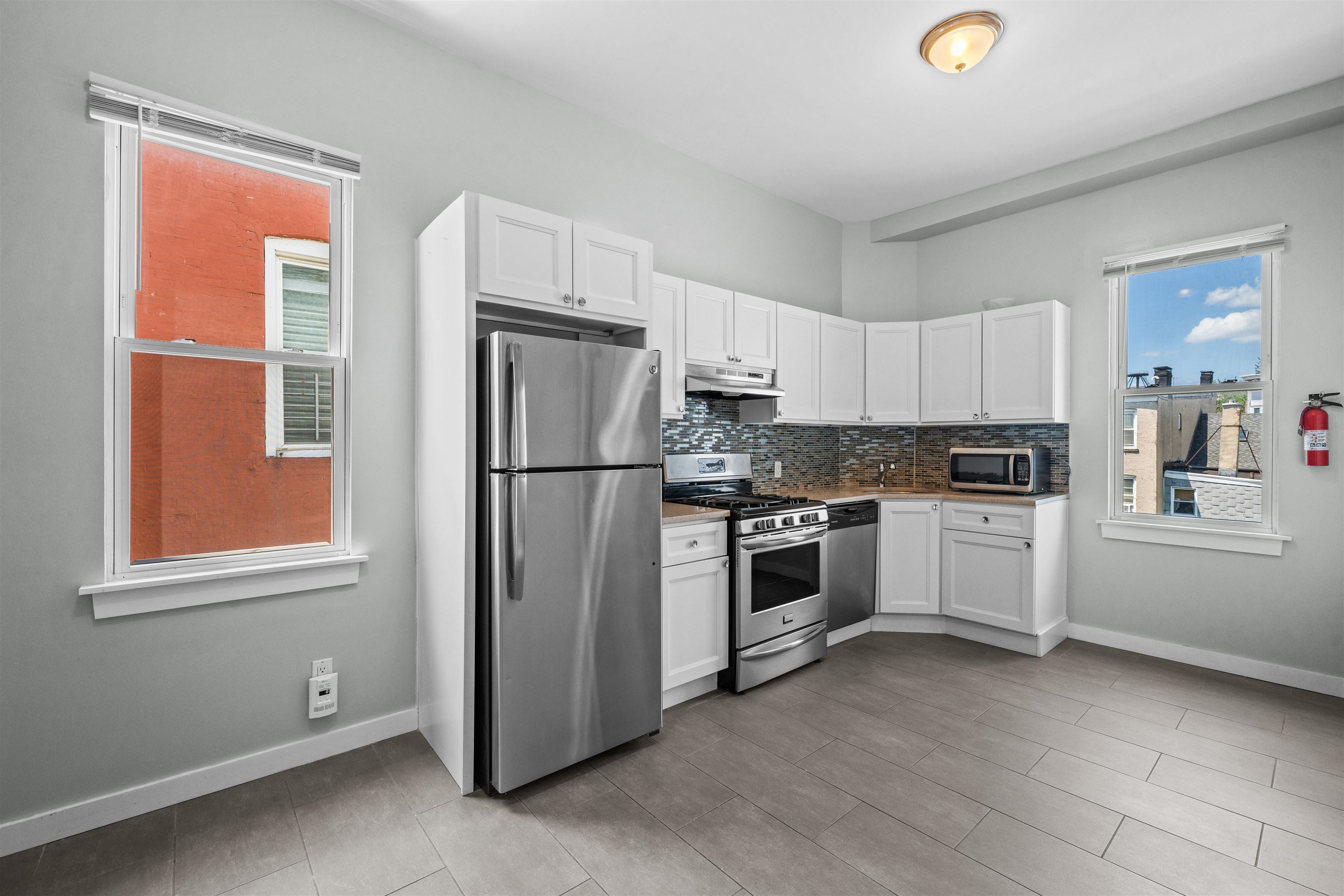Vacant kitchen with white cabinets, stainless steel appliances, and a multicolored tile backsplash.