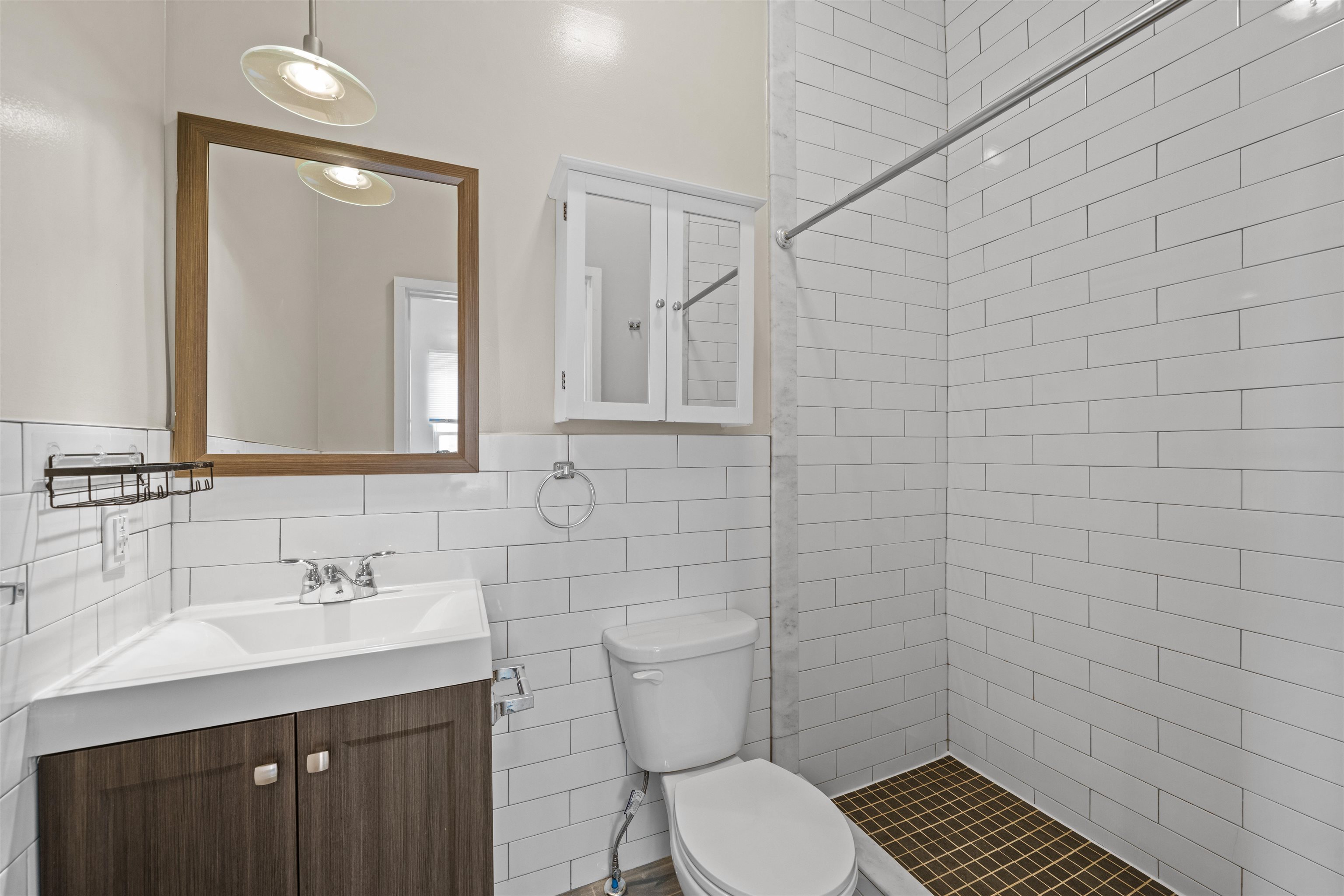 Bathroom with white subway tile, a dark grid-pattern shower floor, and a wood vanity.
