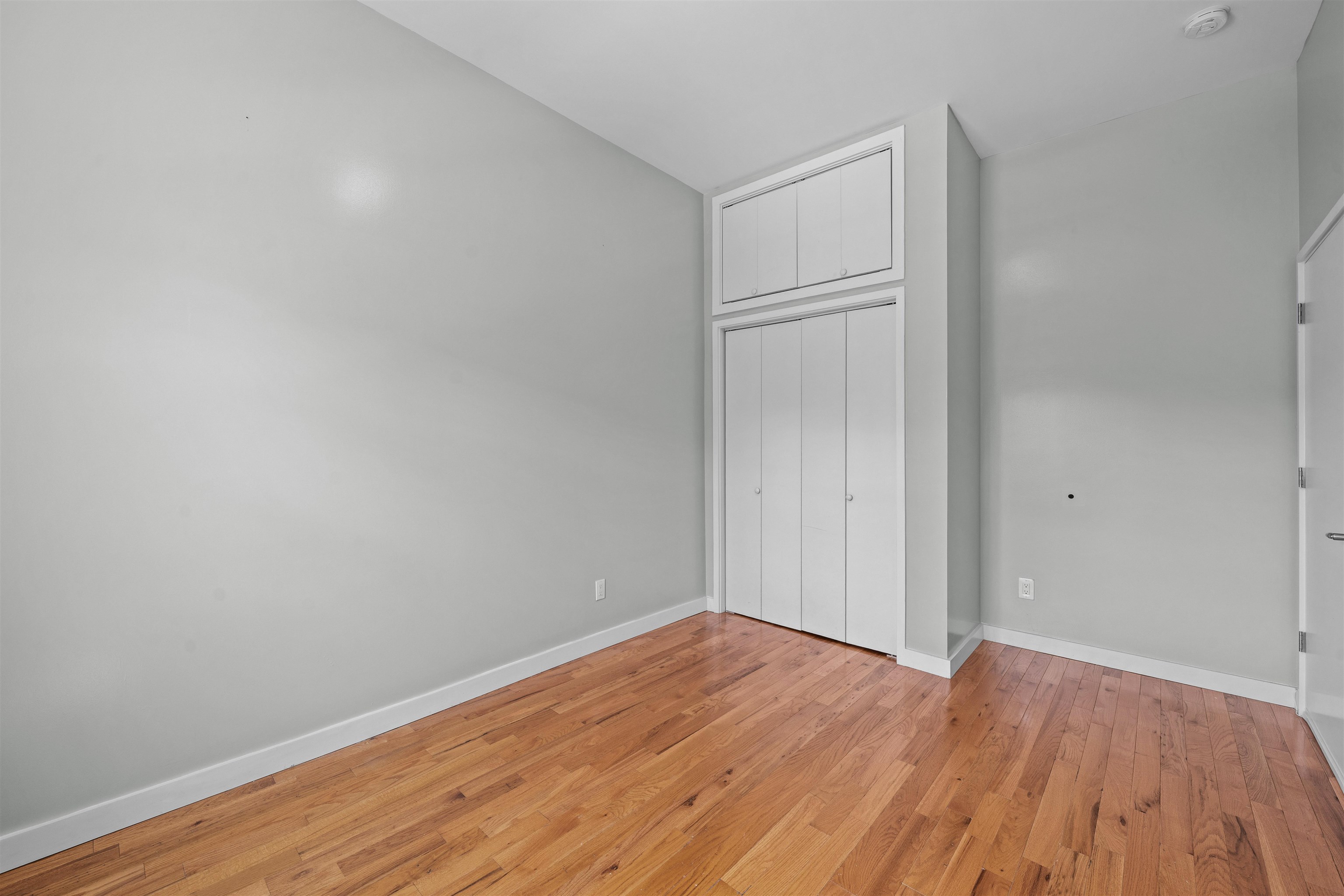 Empty room with hardwood floors and built-in closets with overhead storage.
