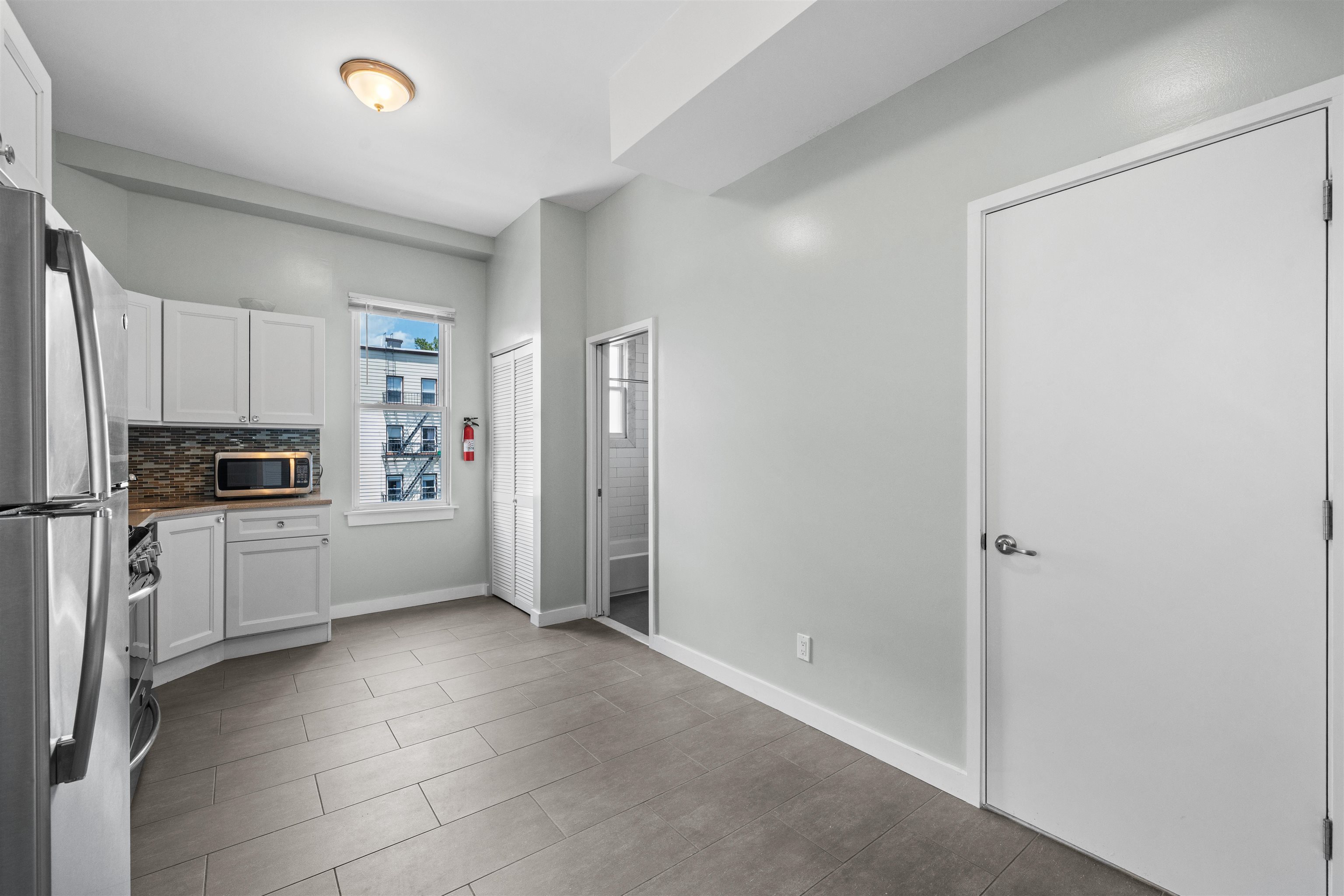 Vacant kitchen with white cabinets, stainless-steel appliances, and a mosaic tile backsplash.
