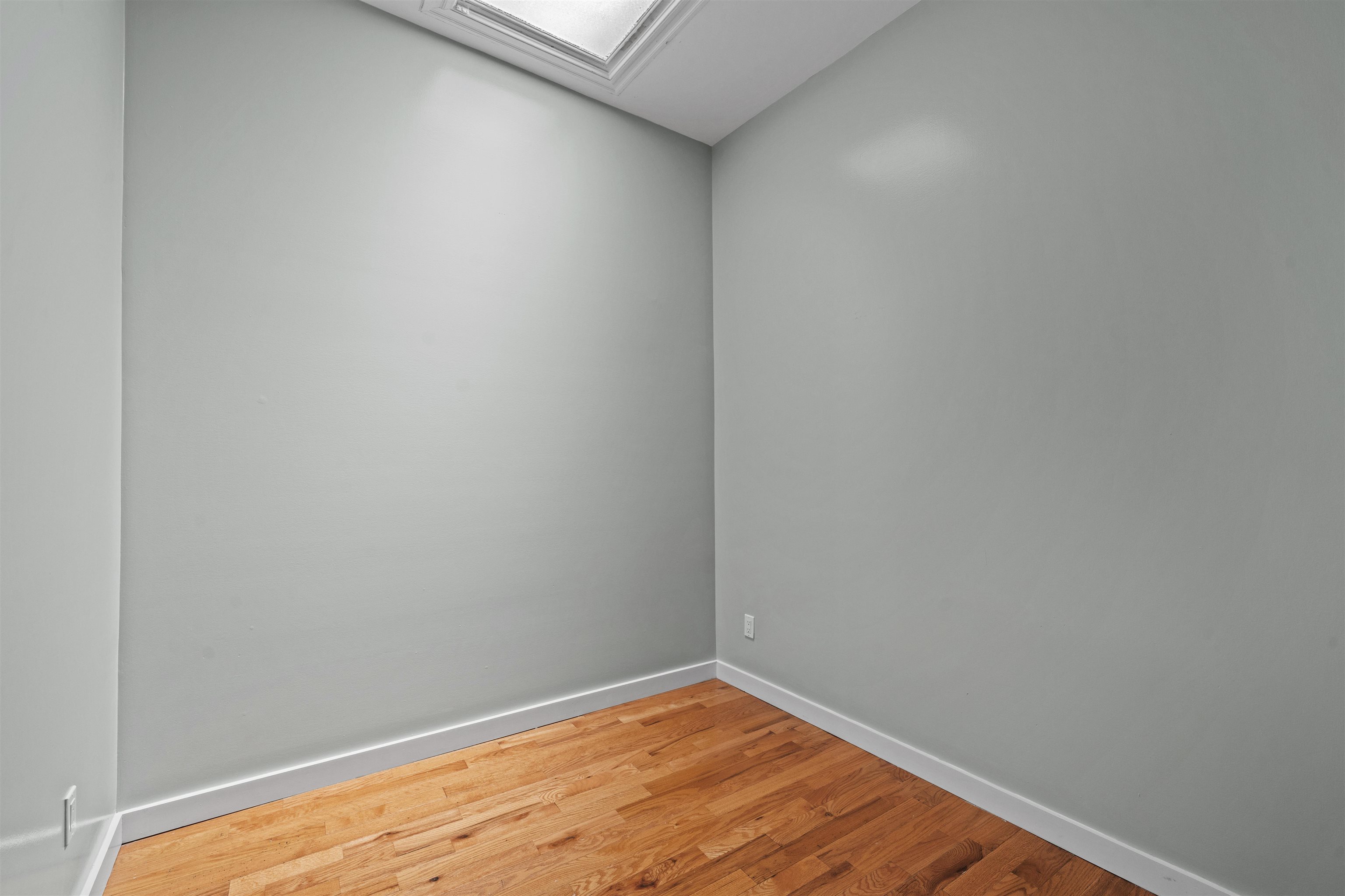 Empty room with hardwood flooring and a skylight.