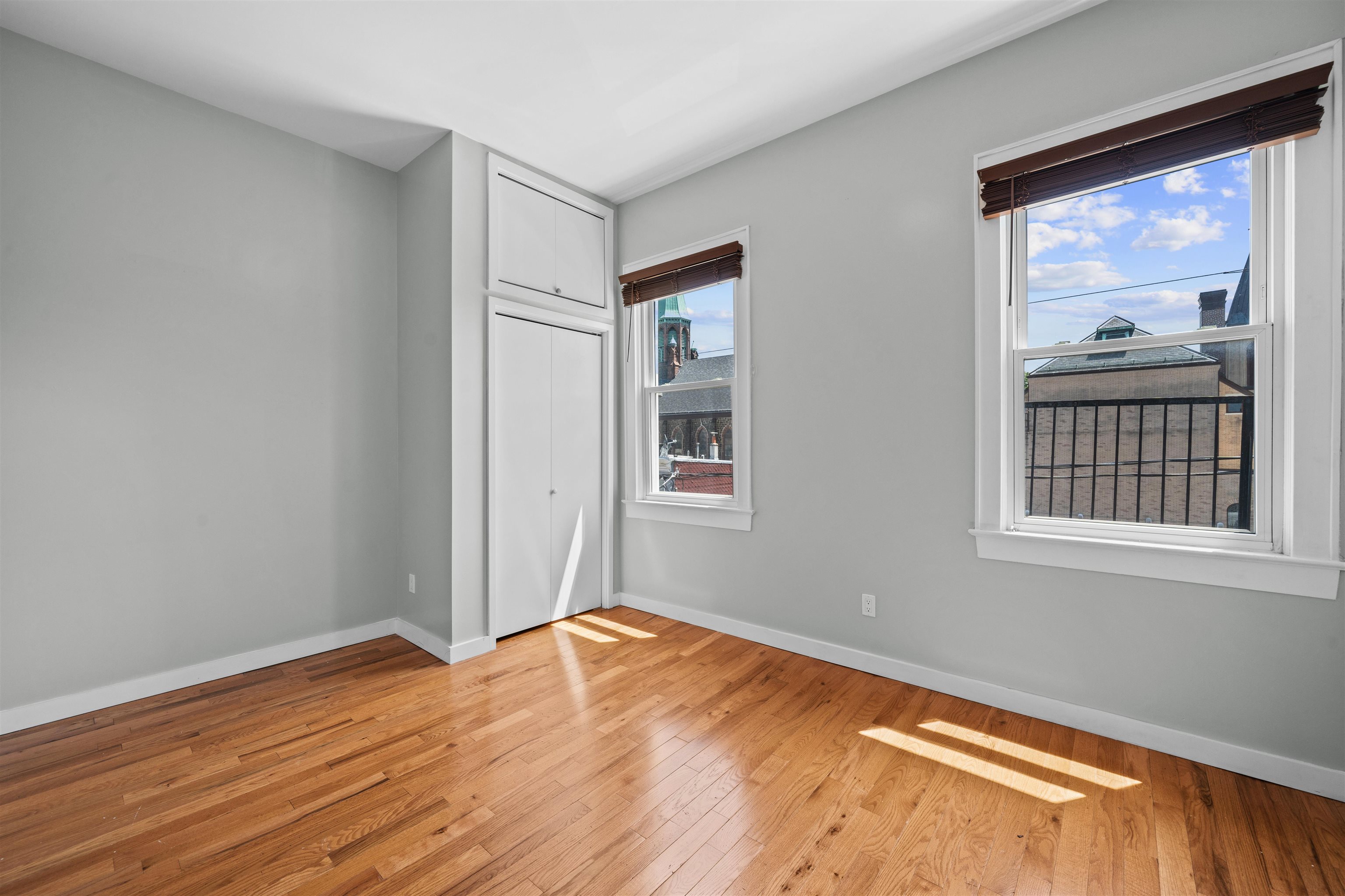 Empty room with hardwood floors, built-in closet, and windows overlooking rooftops and a church tower.