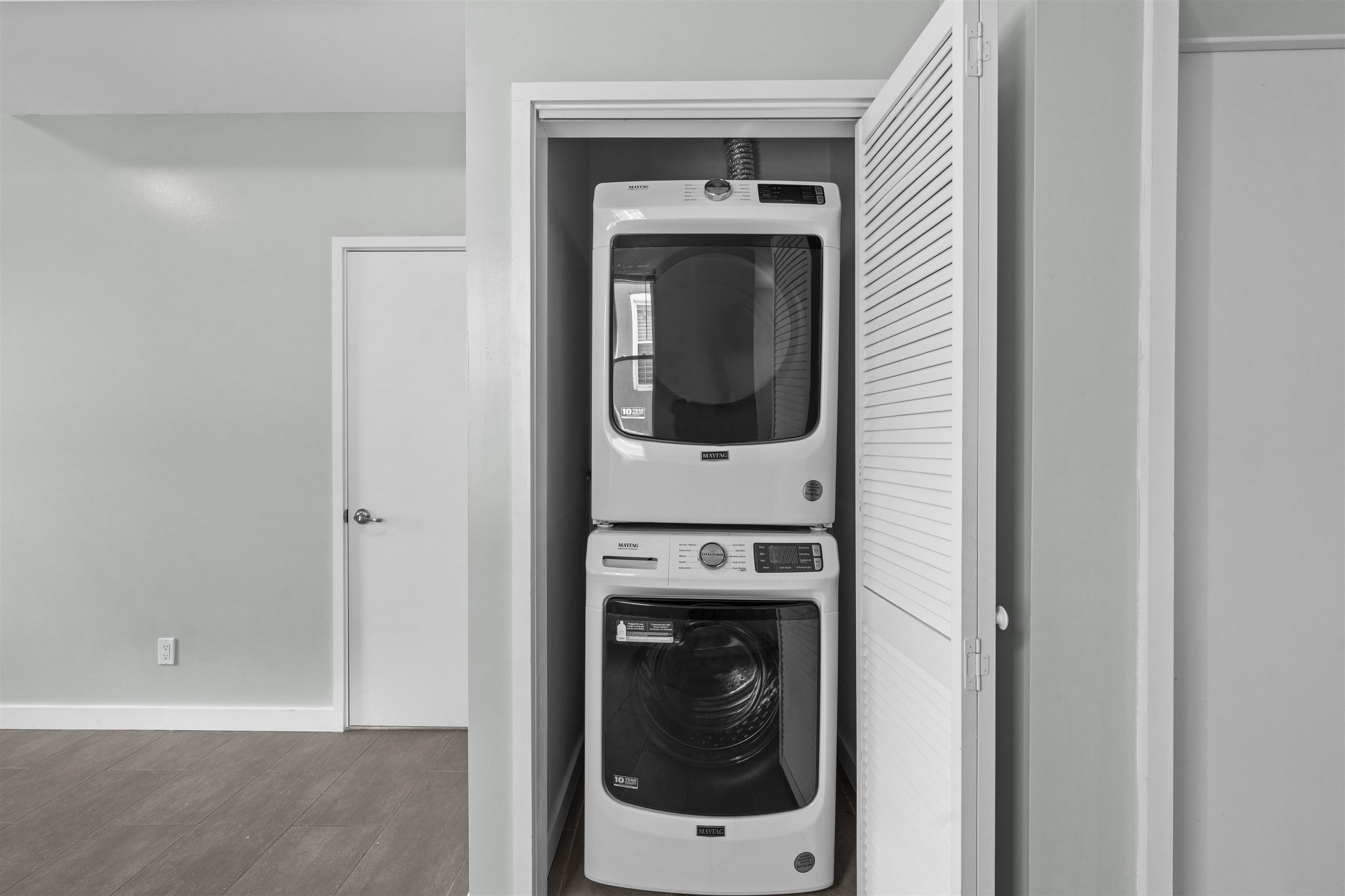Stacked Maytag washer and dryer in a laundry closet behind an open louvered door.