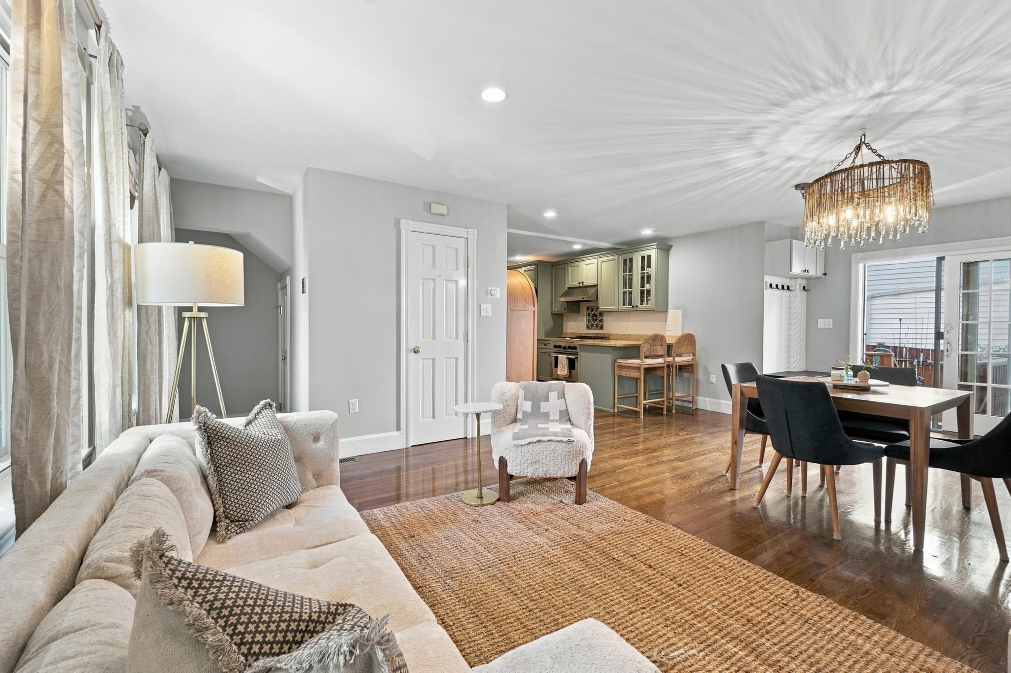 Open-plan living and dining room with green kitchen cabinets, hardwood floors, and a glass door to the balcony.