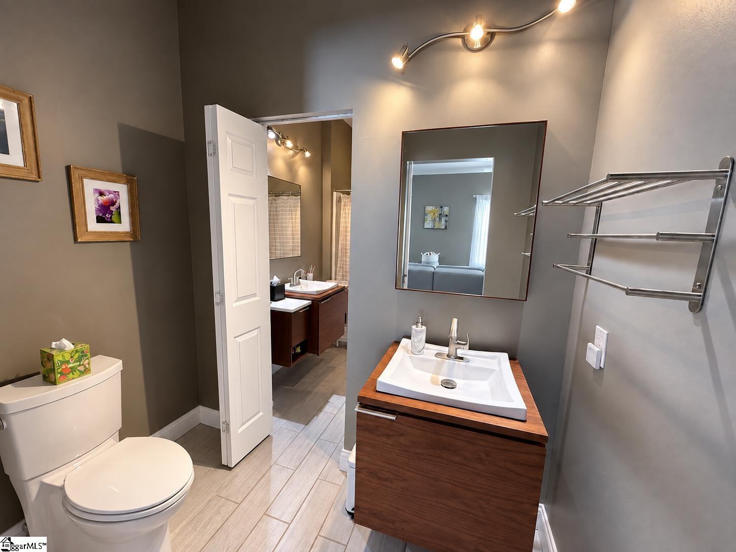 Bathroom with a wood vanity, vessel sink, large mirror, and doorway to a second vanity.