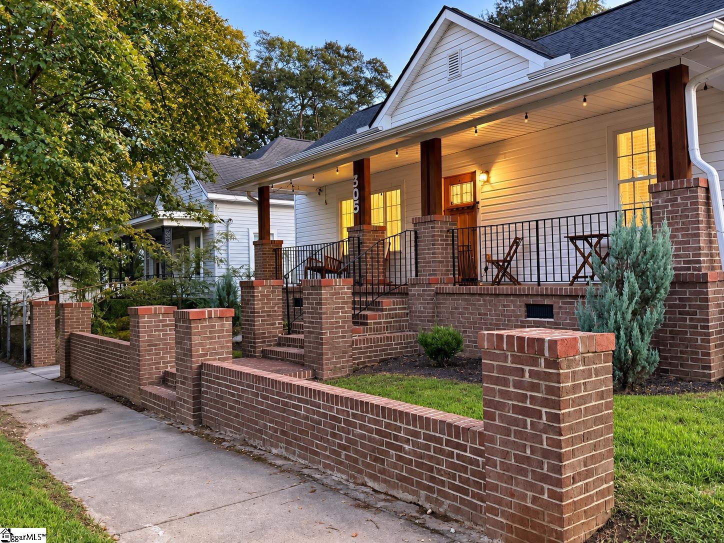 White-sided home with a raised brick porch, black railings, and warm lights at dusk.