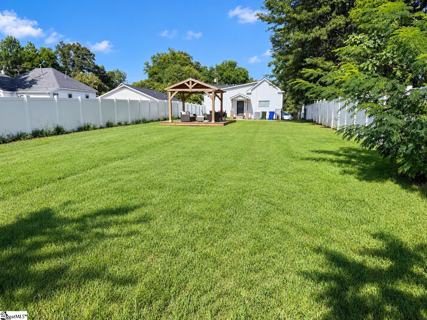 Fenced backyard with a broad green lawn and timber pavilion beside a white house.