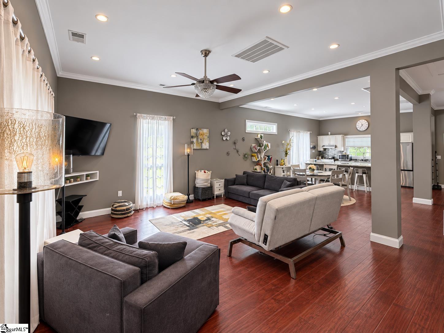 Open-plan living room with gray sofas, dark wood floors, and a view into the dining area and kitchen.