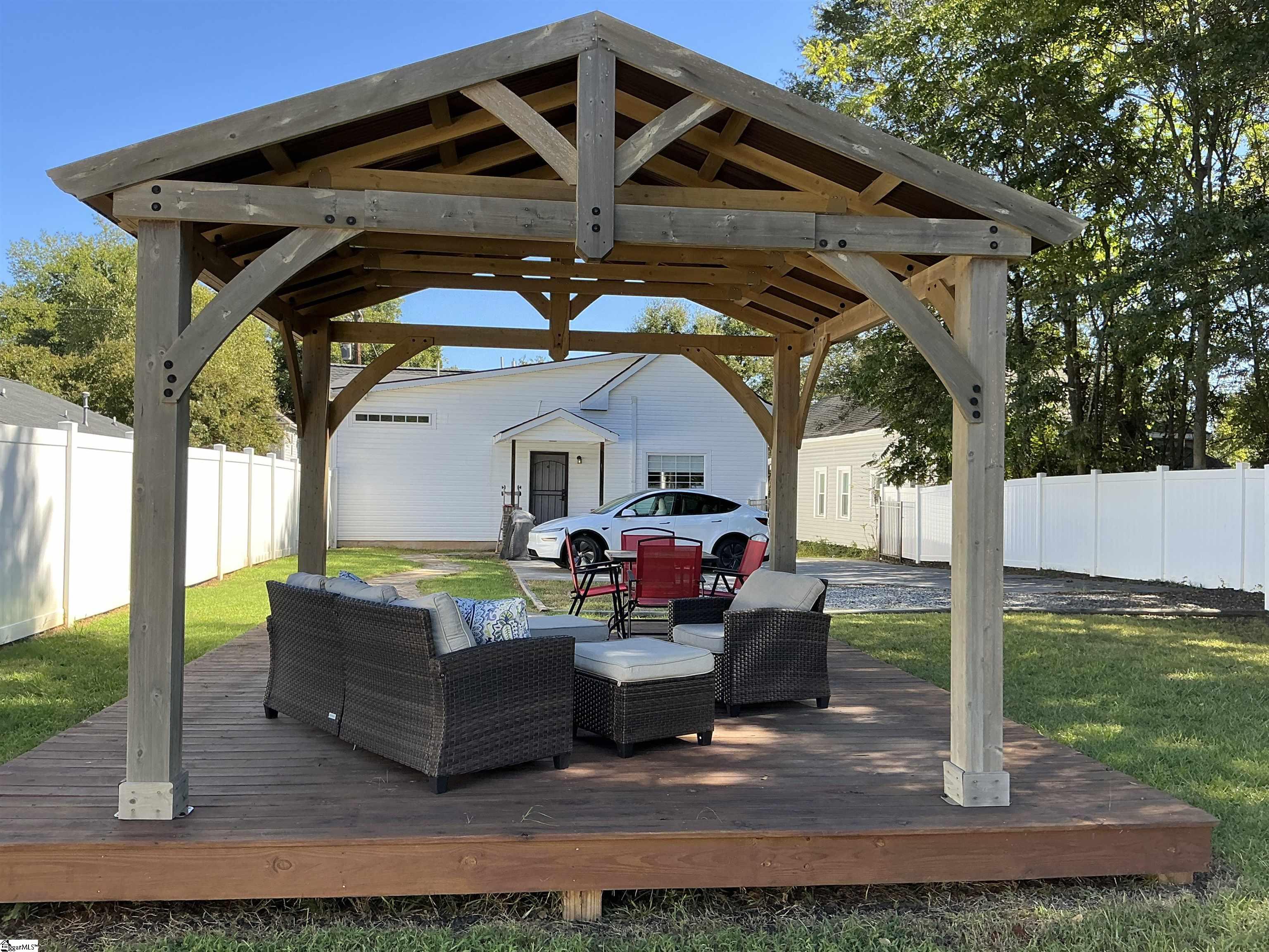Backyard deck with a timber pergola, wicker seating, and a white house beyond.