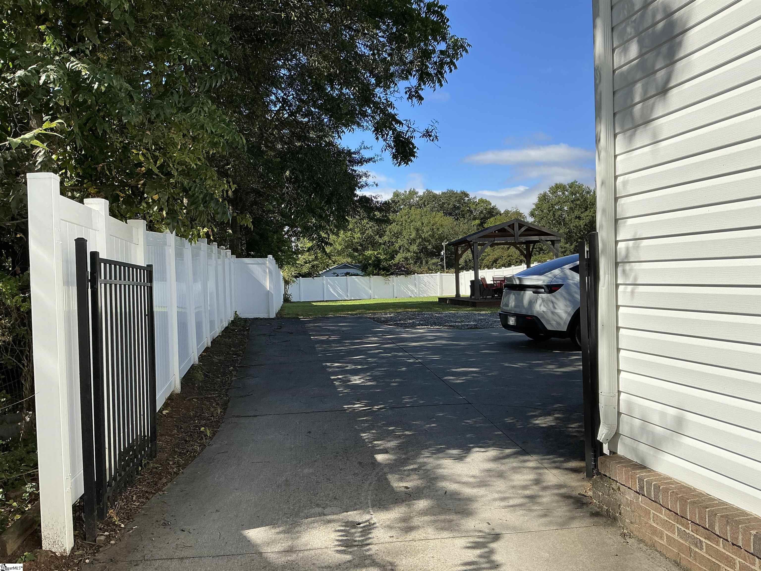 Fenced driveway and yard beside a white-sided home, with a covered patio gazebo.