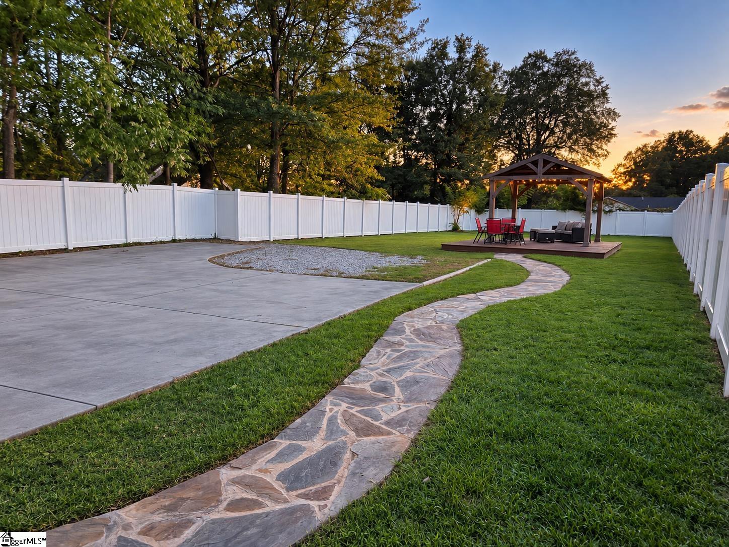 Fenced backyard with a curved stone path leading to a gazebo and outdoor seating.