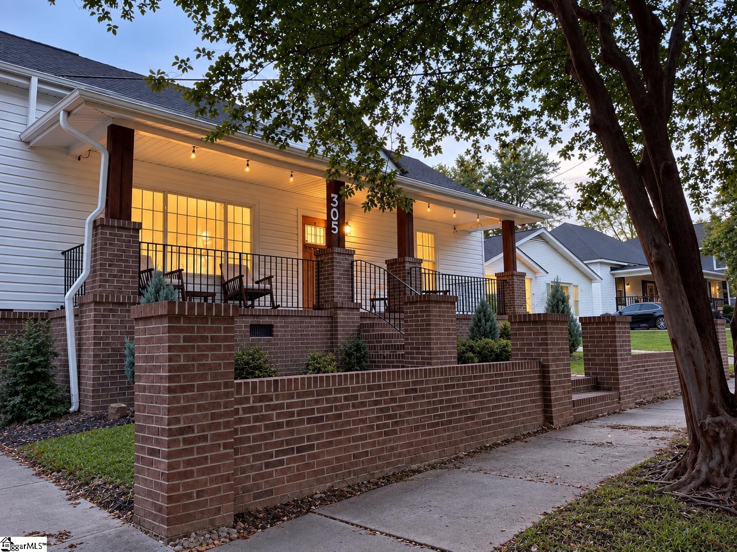 White-sided home with a covered, illuminated porch behind a low brick wall.