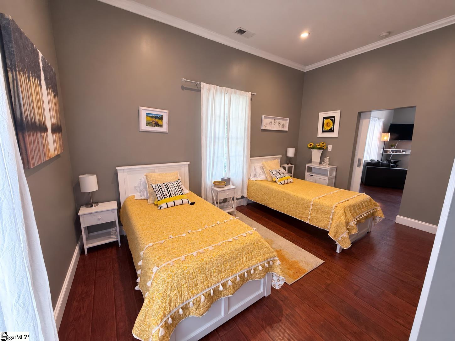 Staged bedroom with two twin beds dressed in yellow bedding and a doorway to the living area.