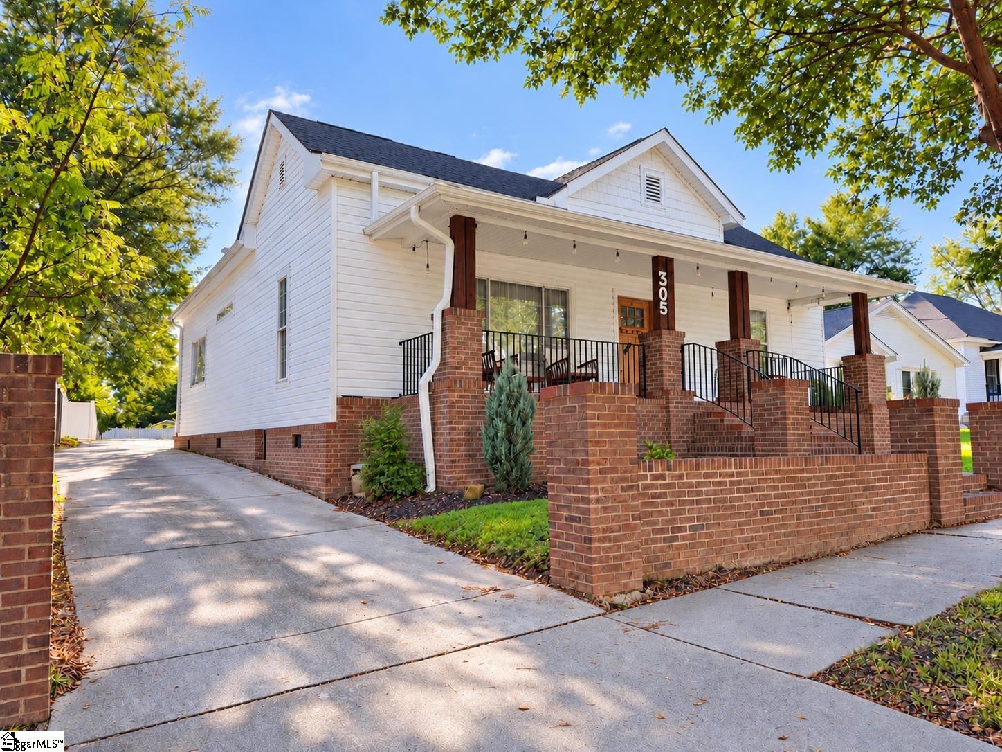 White-sided house with a brick porch, black railings, and a wide paved driveway.