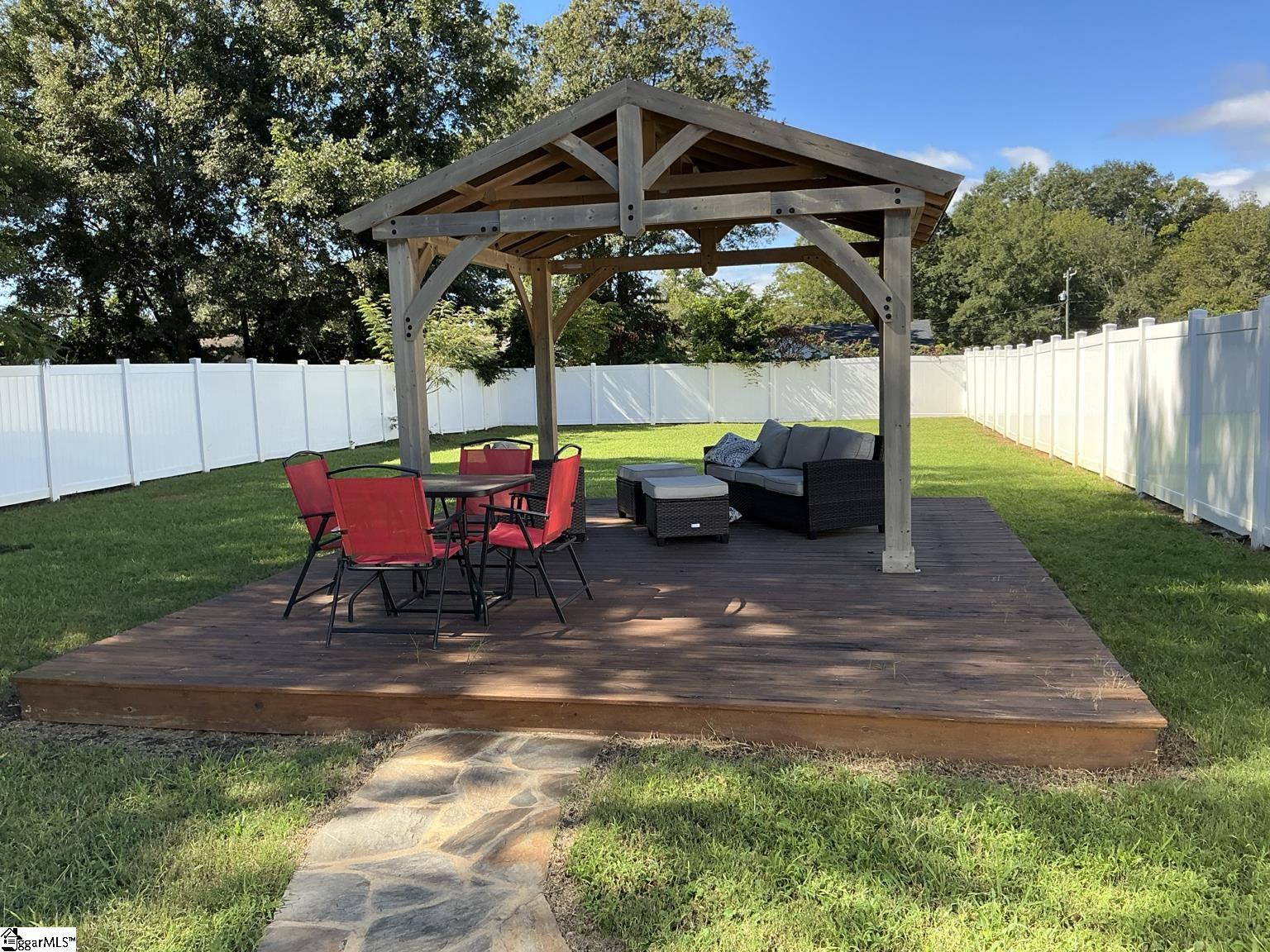 Backyard deck with a timber pavilion, red dining chairs, gray lounge seating, and a white privacy fence.
