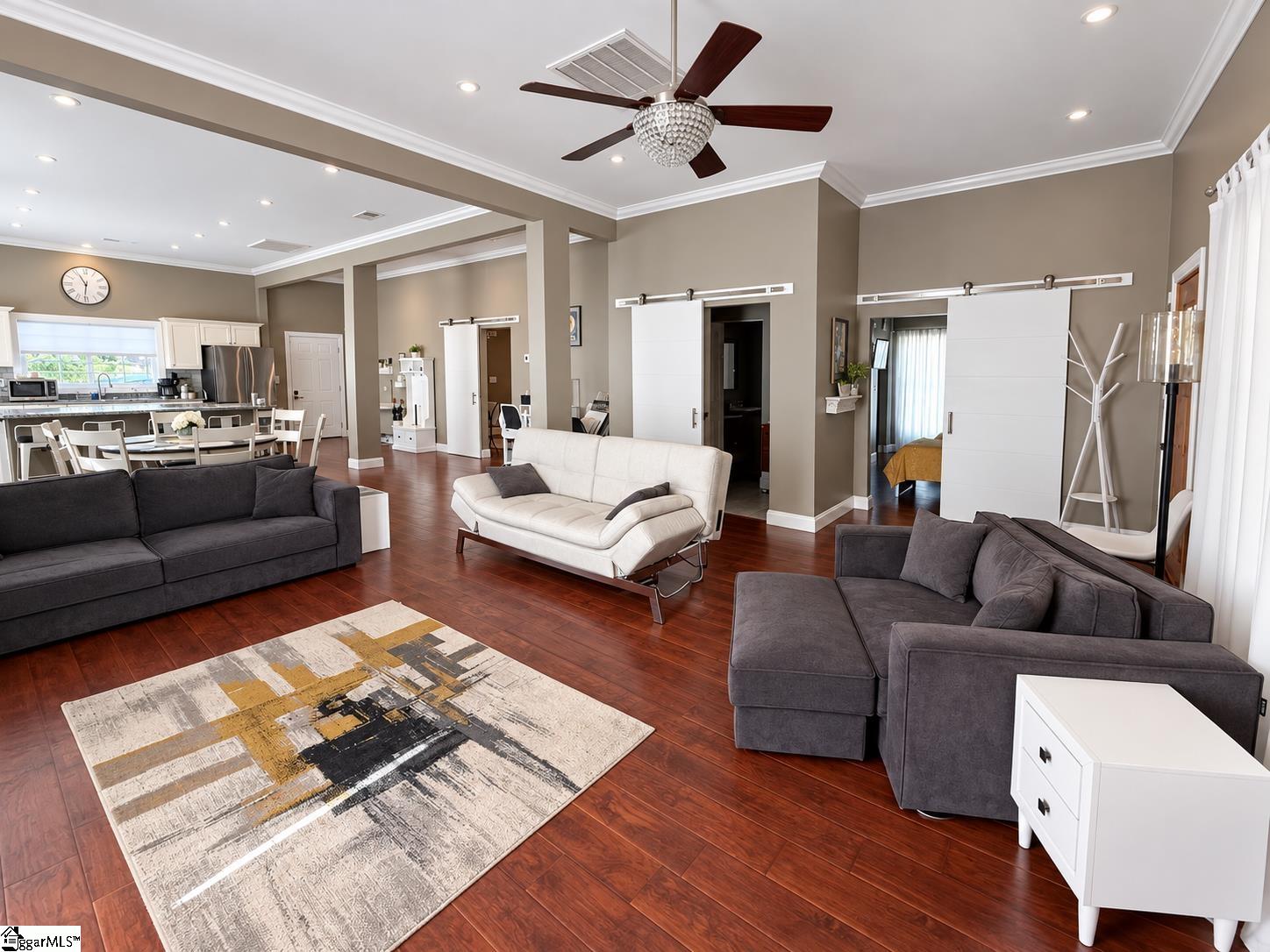 Open-plan living room with gray and white sofas, dark hardwood floors, and white sliding barn doors.