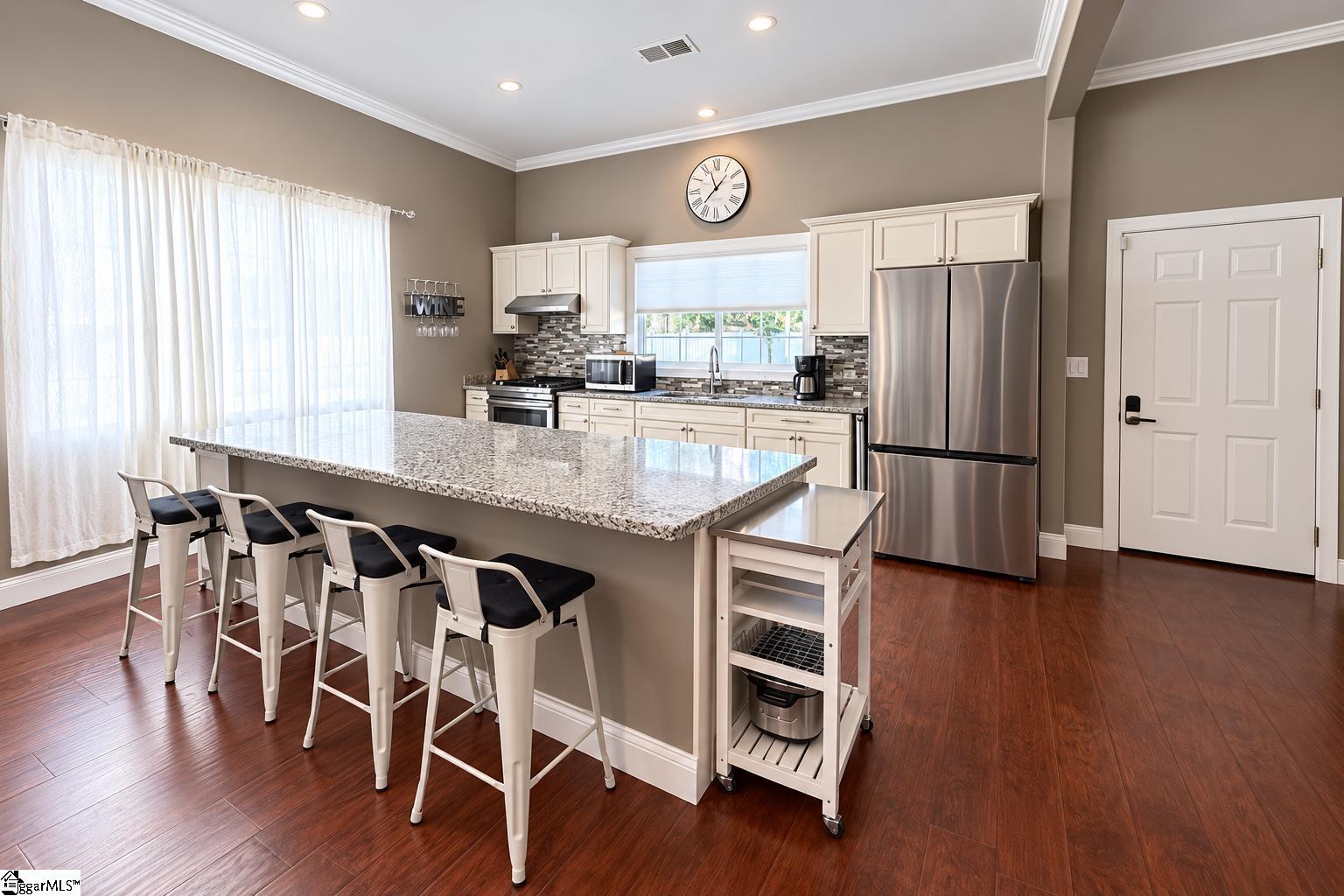 Kitchen with a large stone island, white cabinetry, stainless steel appliances, and dark wood floors.