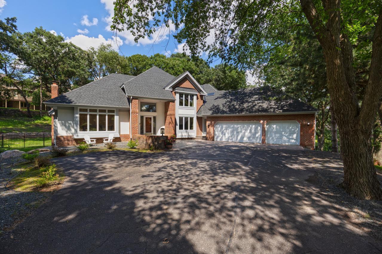 Brick-and-gray home with a two-car garage, broad driveway, and mature trees shading the front yard.