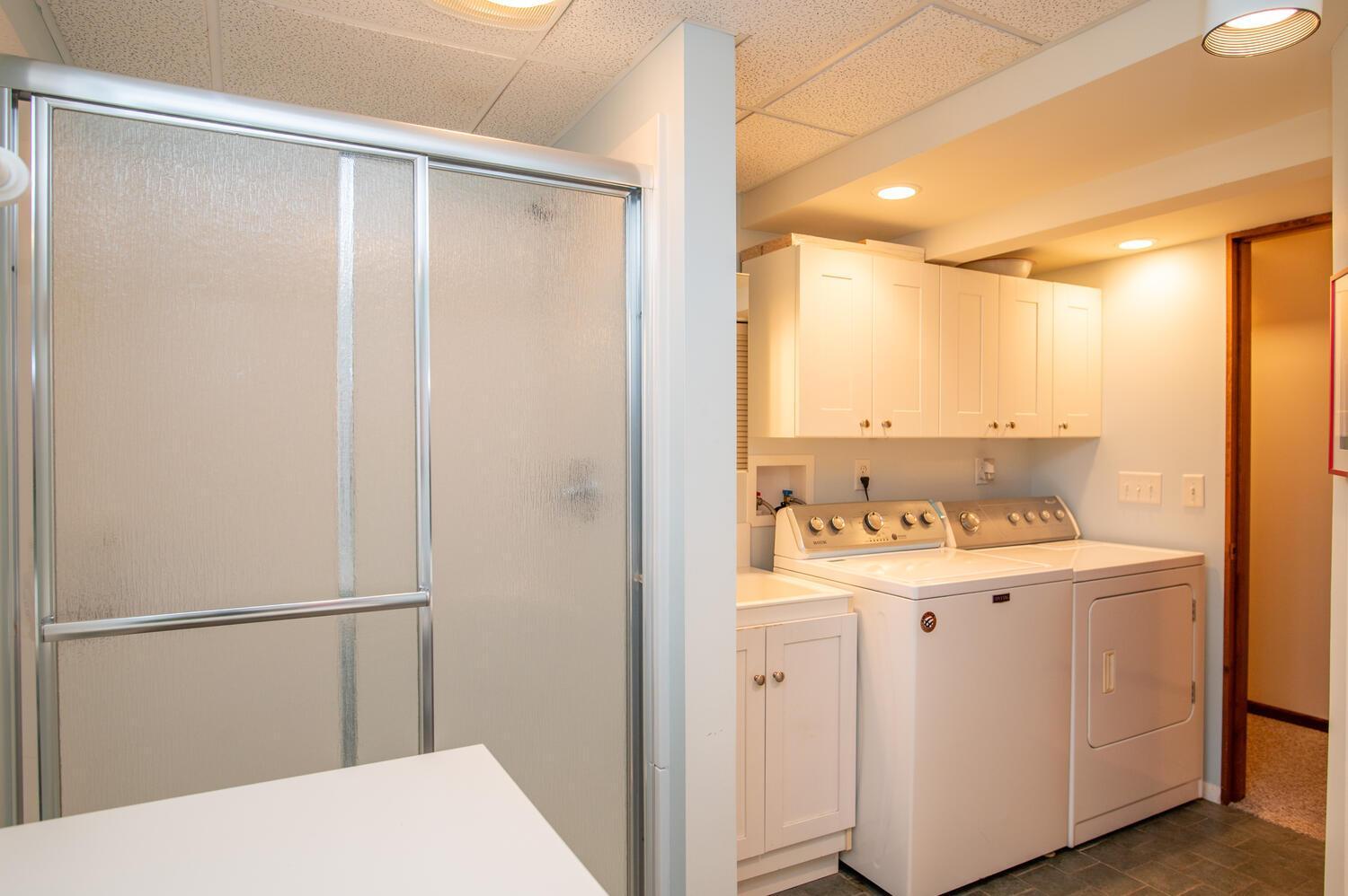 Laundry room with white washer and dryer, upper cabinets, and a frosted-glass shower enclosure.