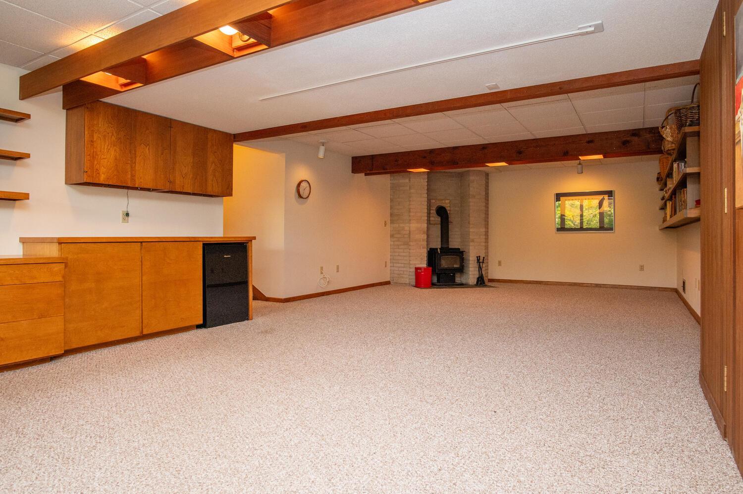 Unfurnished carpeted basement room with built-in wood cabinetry and a wood-burning stove.