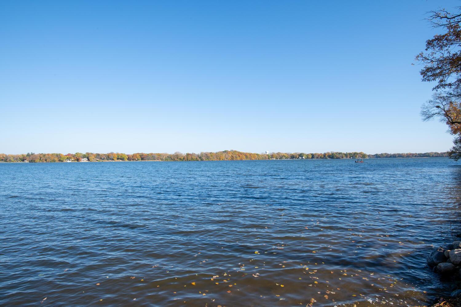 Panoramic lake view with autumn foliage along the opposite shore and a small boat.