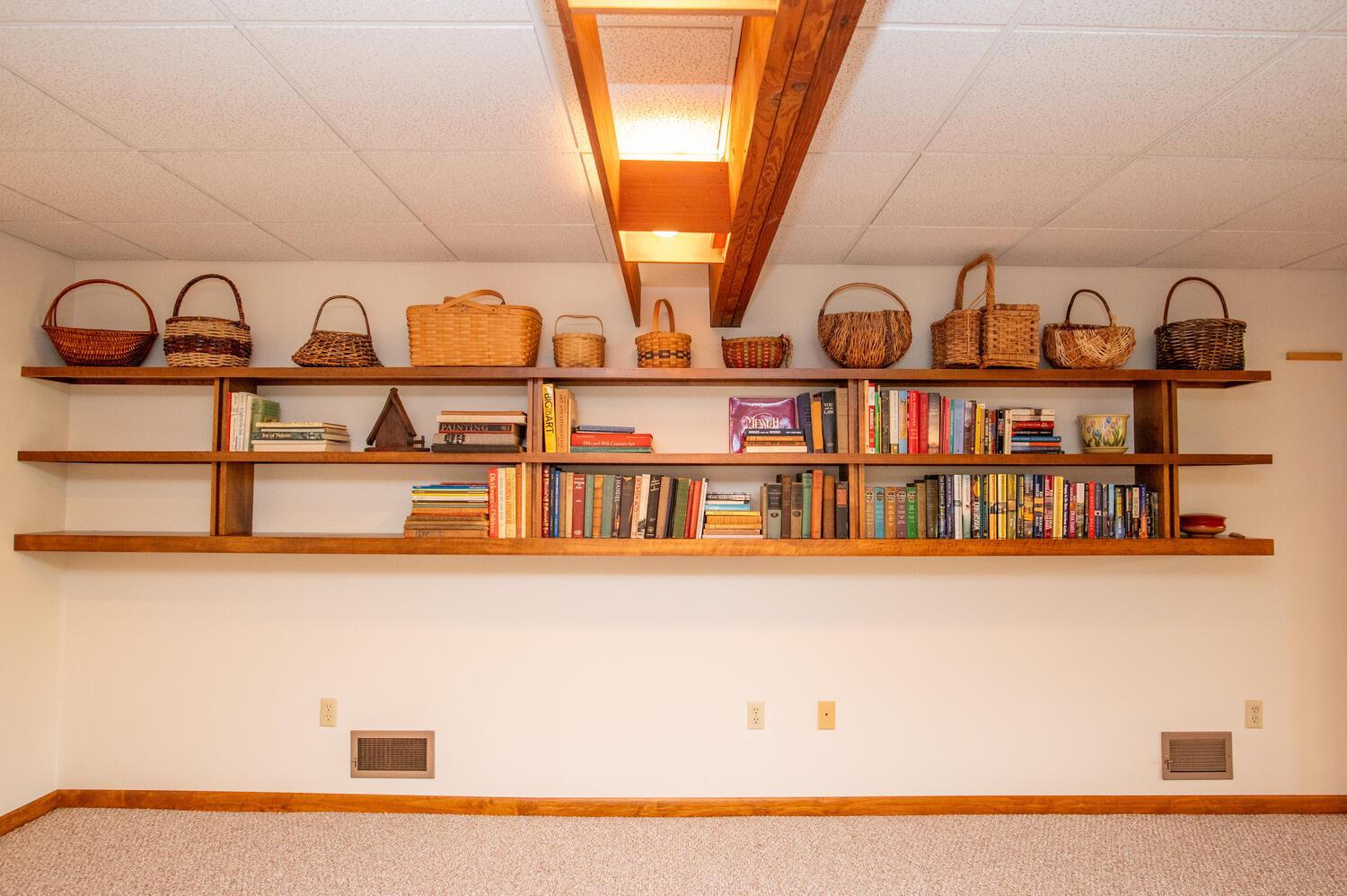 Wooden wall shelves display books and wicker baskets above a carpeted floor.