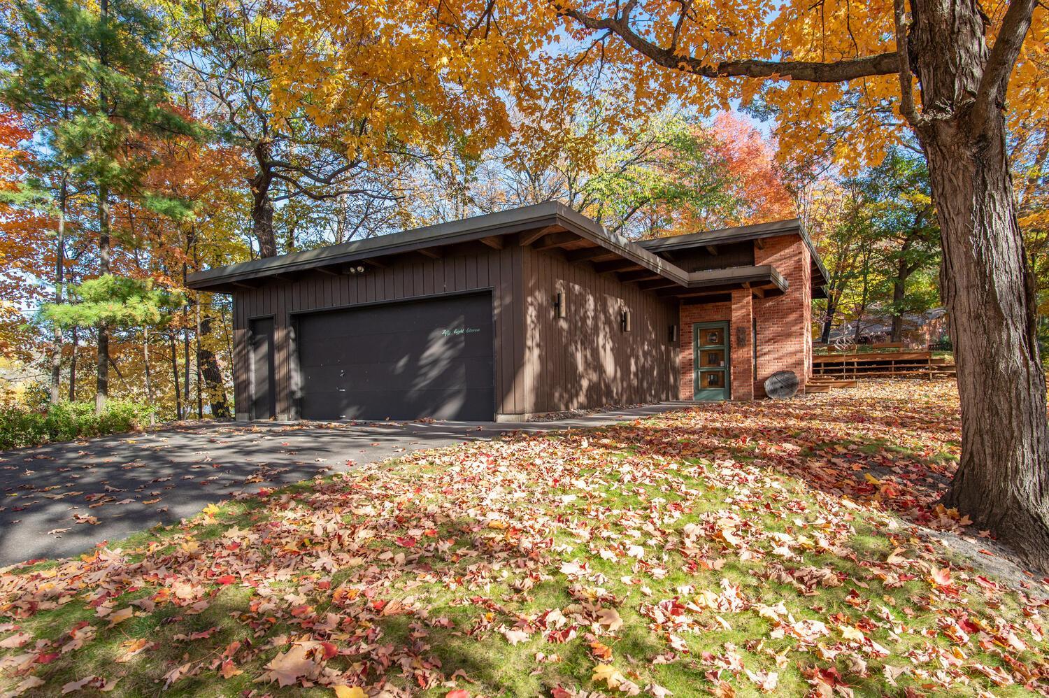 Home with dark wood siding, brick entry, and two-car garage beneath autumn trees.