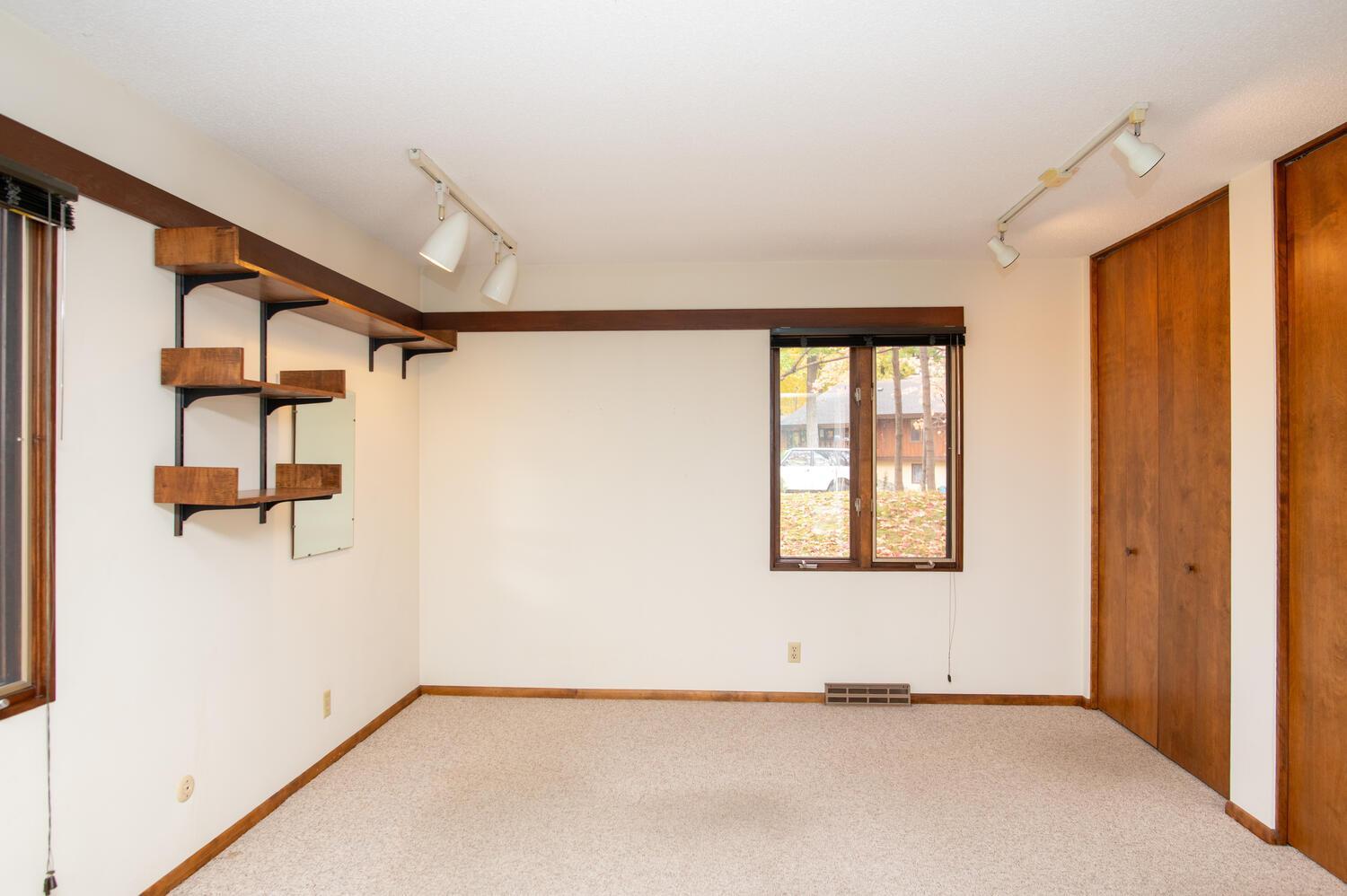 Empty carpeted room with built-in wood shelves and a wall of wooden closet doors.