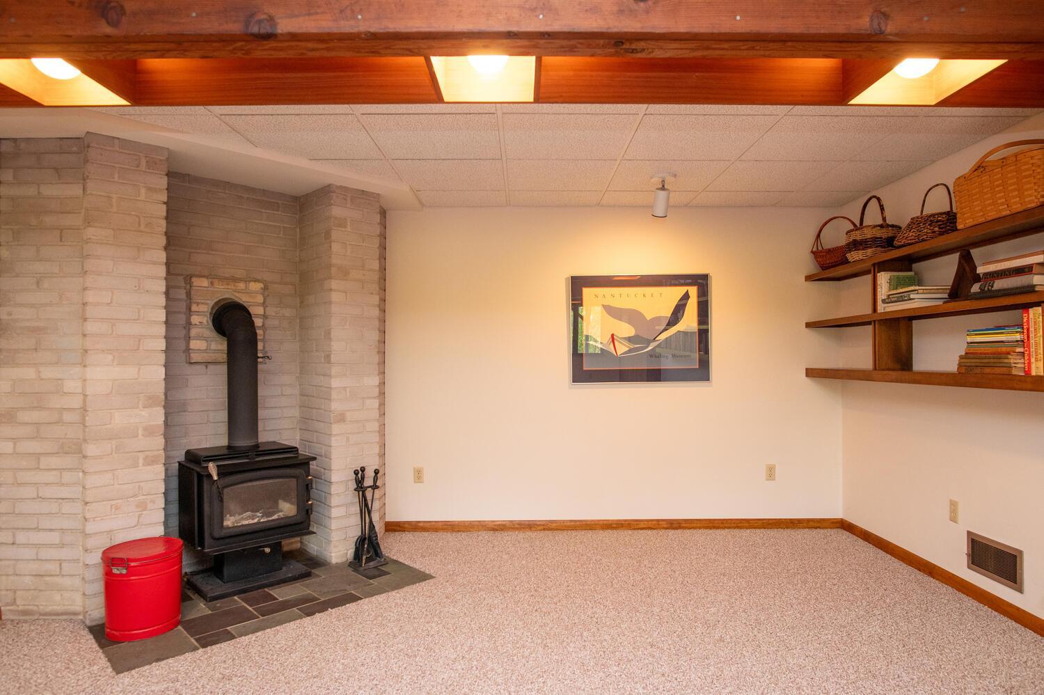 Carpeted room with a black wood stove set into a white brick fireplace and shelves along the wall.